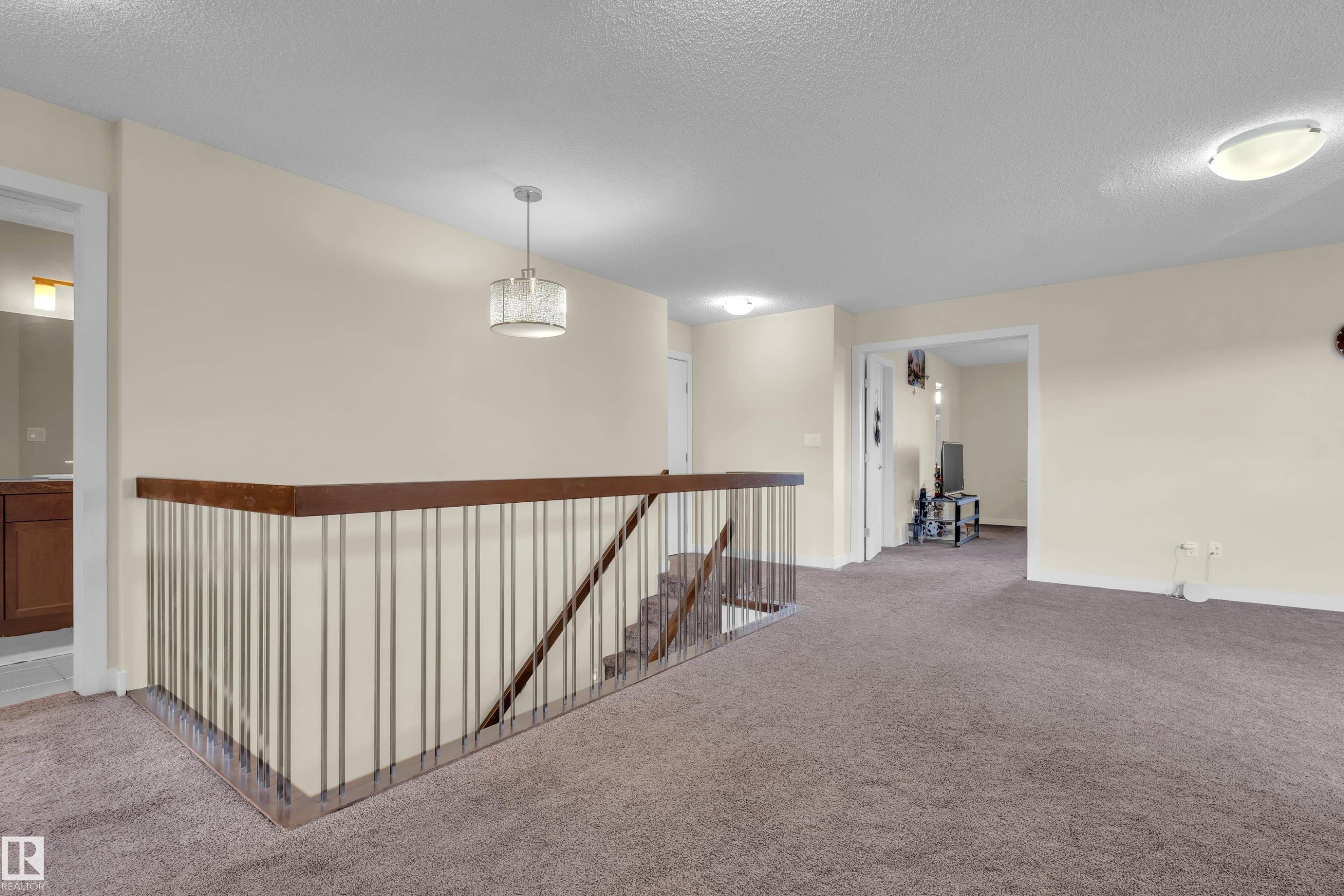 Upper-level landing featuring brown carpeting and a wood-finish handrail with vertical metal balusters - 3071 Carpenter Landing Sw, Edmonton, AB