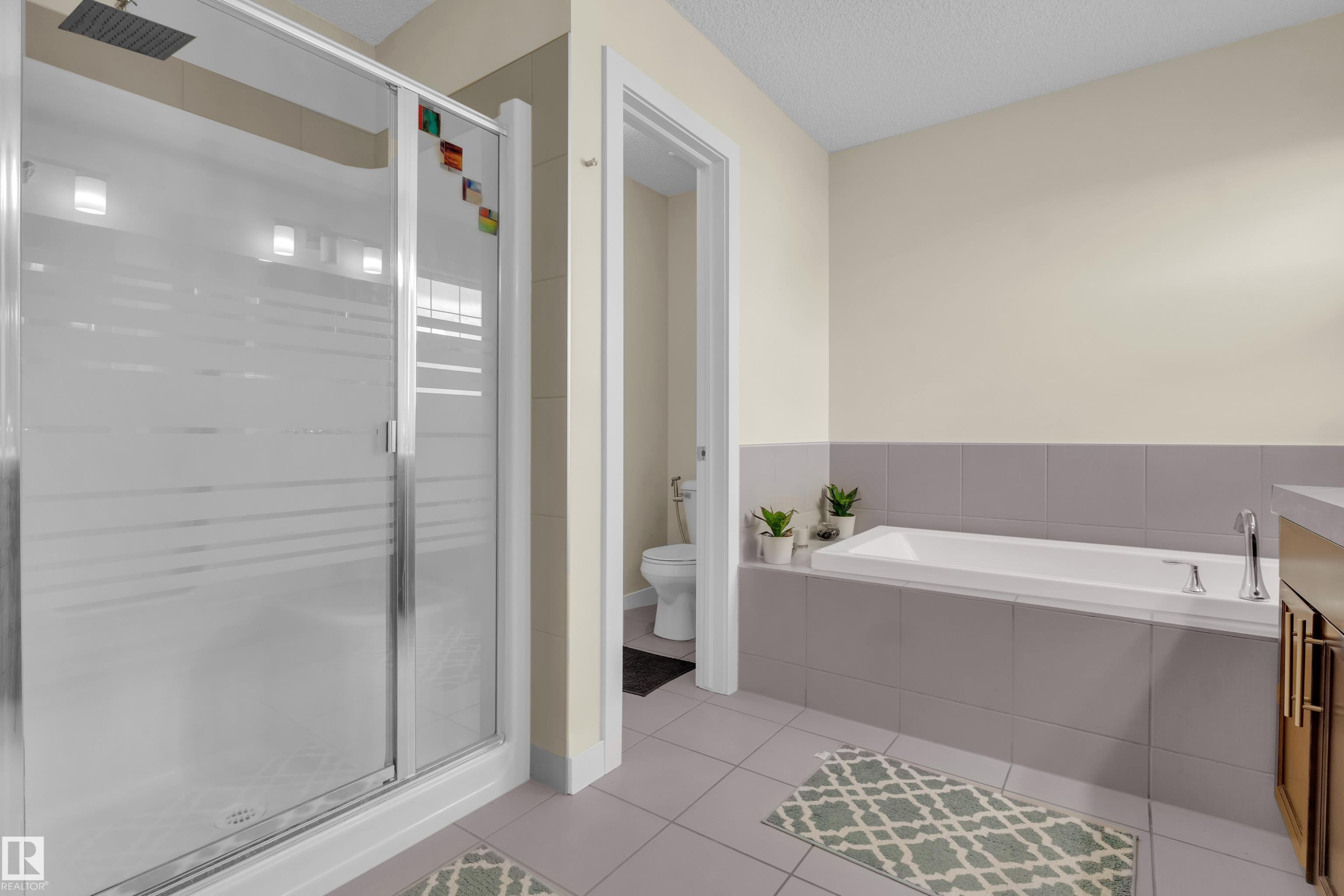 Spacious bathroom featuring a glass-enclosed shower with rainfall showerhead, a large soaking tub, and neutral tiled flooring - 3071 Carpenter Landing Sw, Edmonton, AB