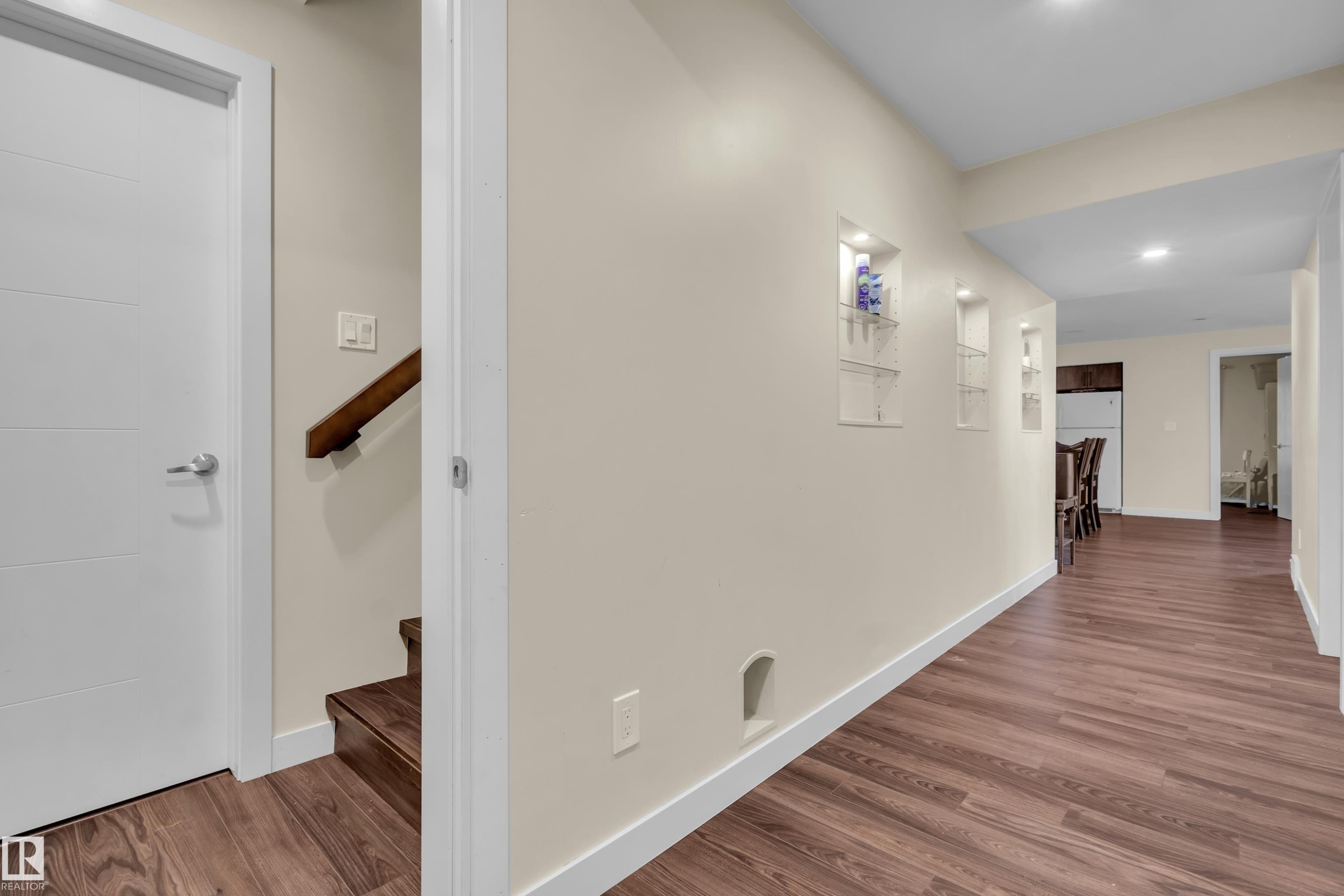 Hallway featuring wood-finish flooring, white baseboards, recessed wall niches, and a neutral paint palette - 3071 Carpenter Landing Sw, Edmonton, AB