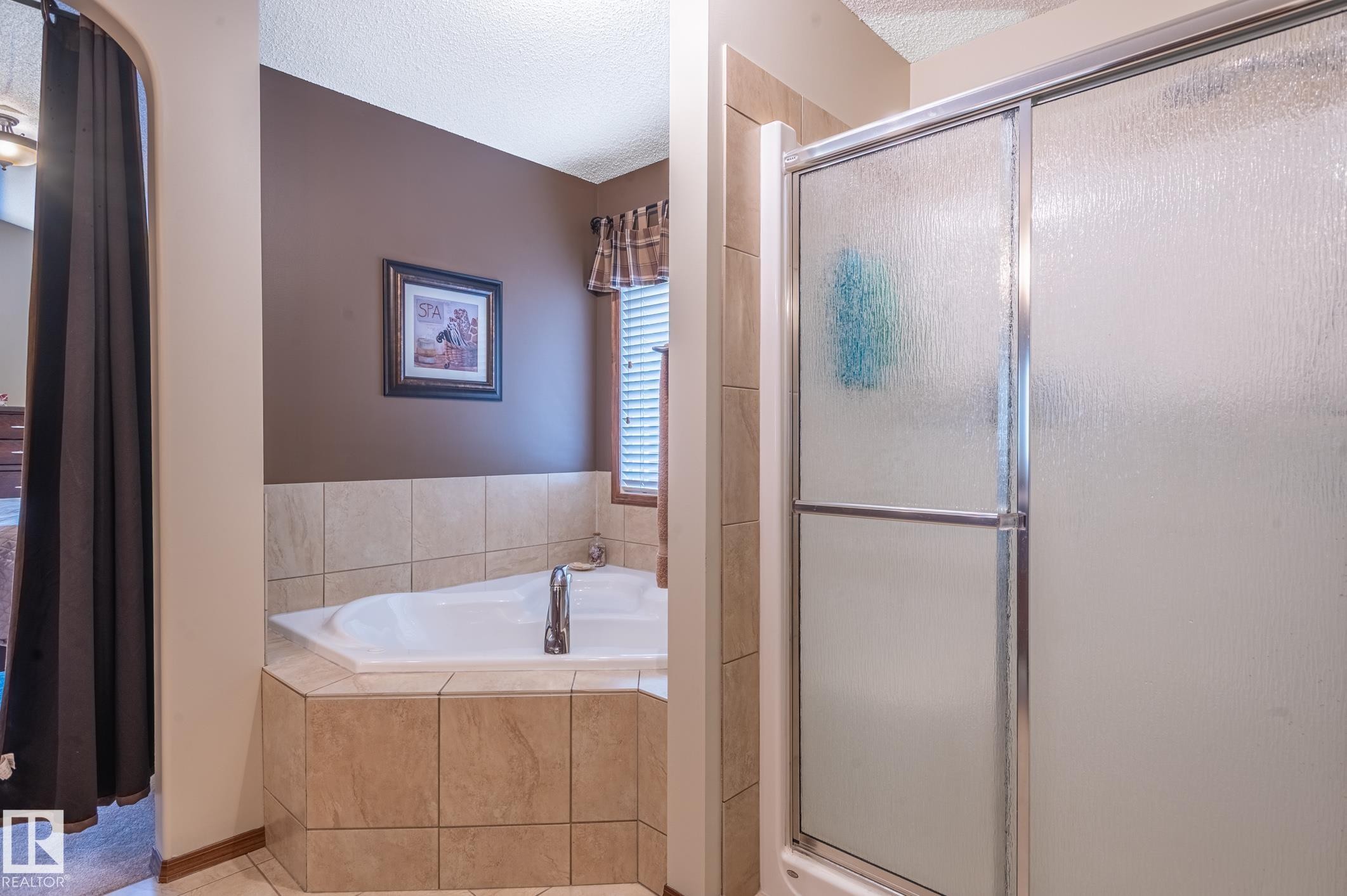 Tiled corner soaking tub with deck-mounted faucet and an enclosed shower with sliding frosted glass doors - 19 Newton Place, St. Albert, AB