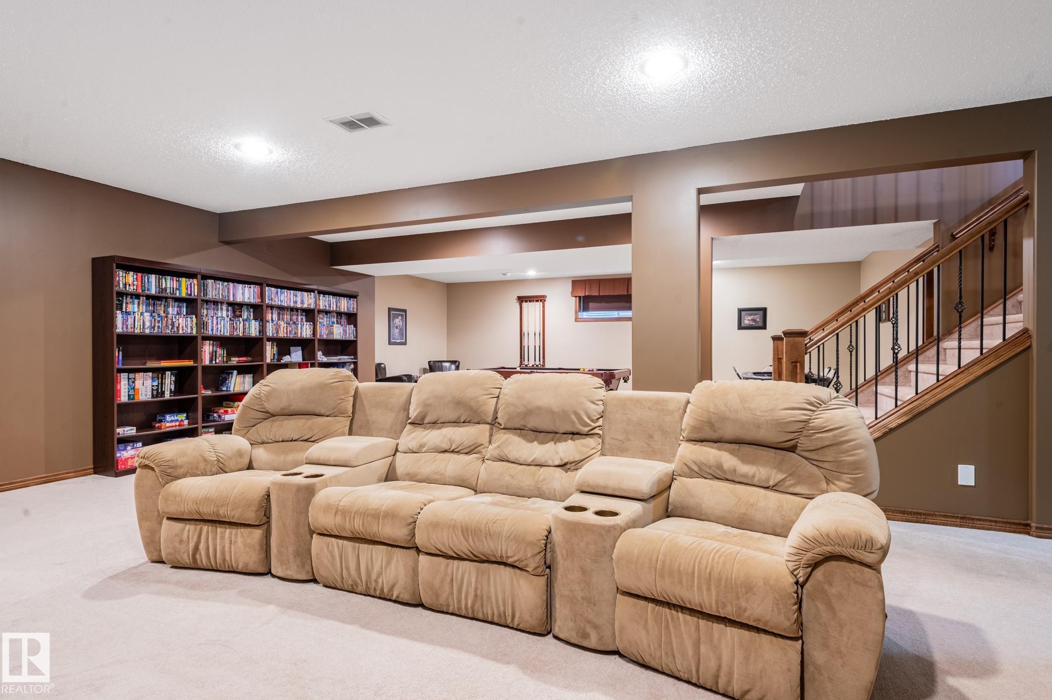 Carpeted lower level featuring recessed lighting, a full-wall built-in bookshelf, and a wood staircase with wrought iron balusters - 19 Newton Place, St. Albert, AB