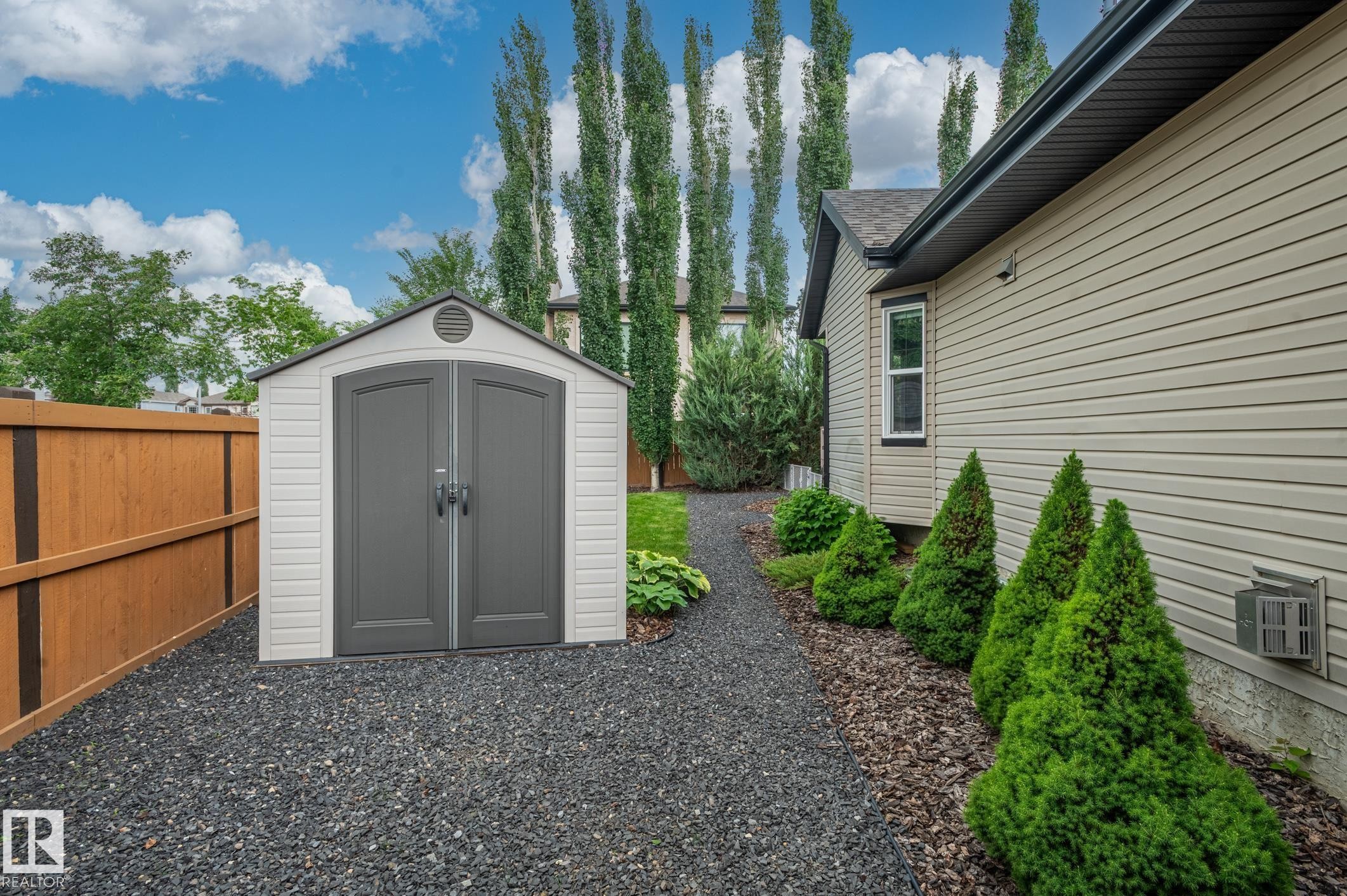 Gravel pathway leading to a two-tone storage shed with arched double doors - 19 Newton Place, St. Albert, AB