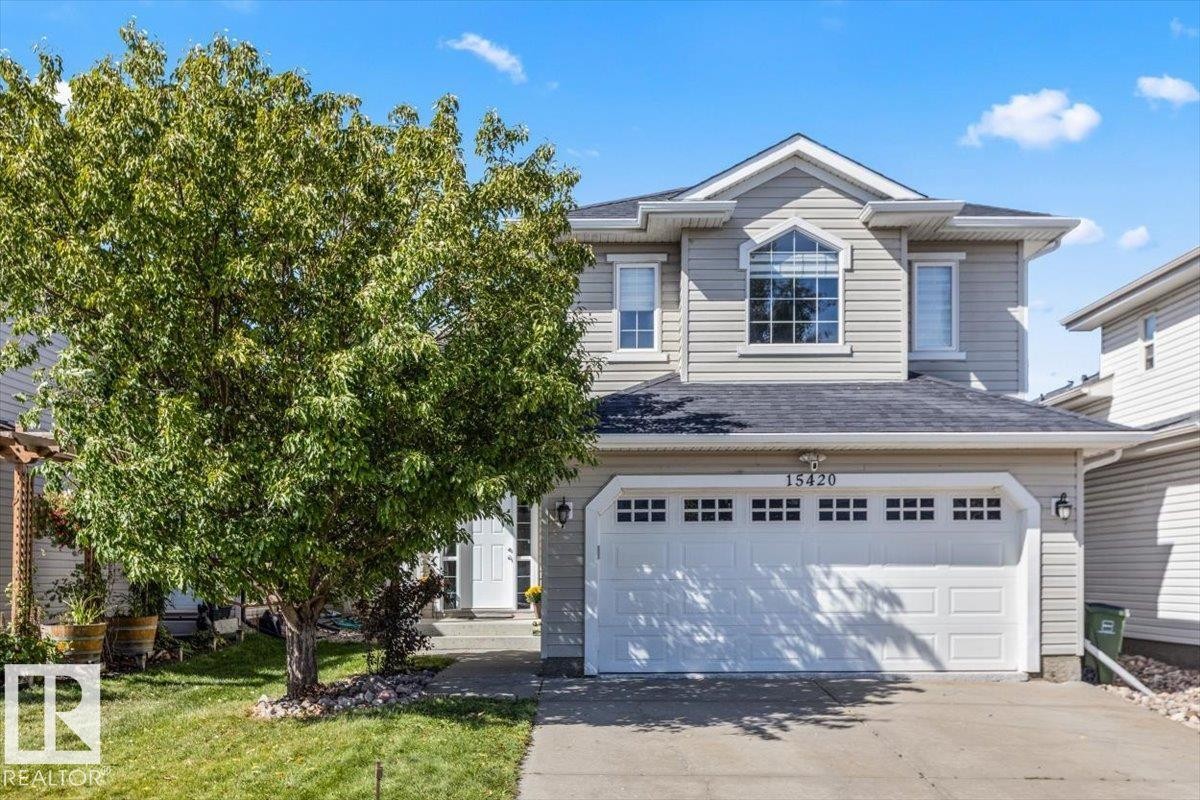 Two-story property with light-colored siding, a two-car garage, and a prominent arched window on the upper level - 15420 44 Street Nw, Edmonton, AB