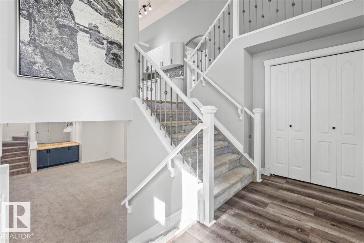 Two-story foyer featuring wood-finish flooring and a carpeted staircase with white railings and wrought iron balusters - 15420 44 Street Nw, Edmonton, AB