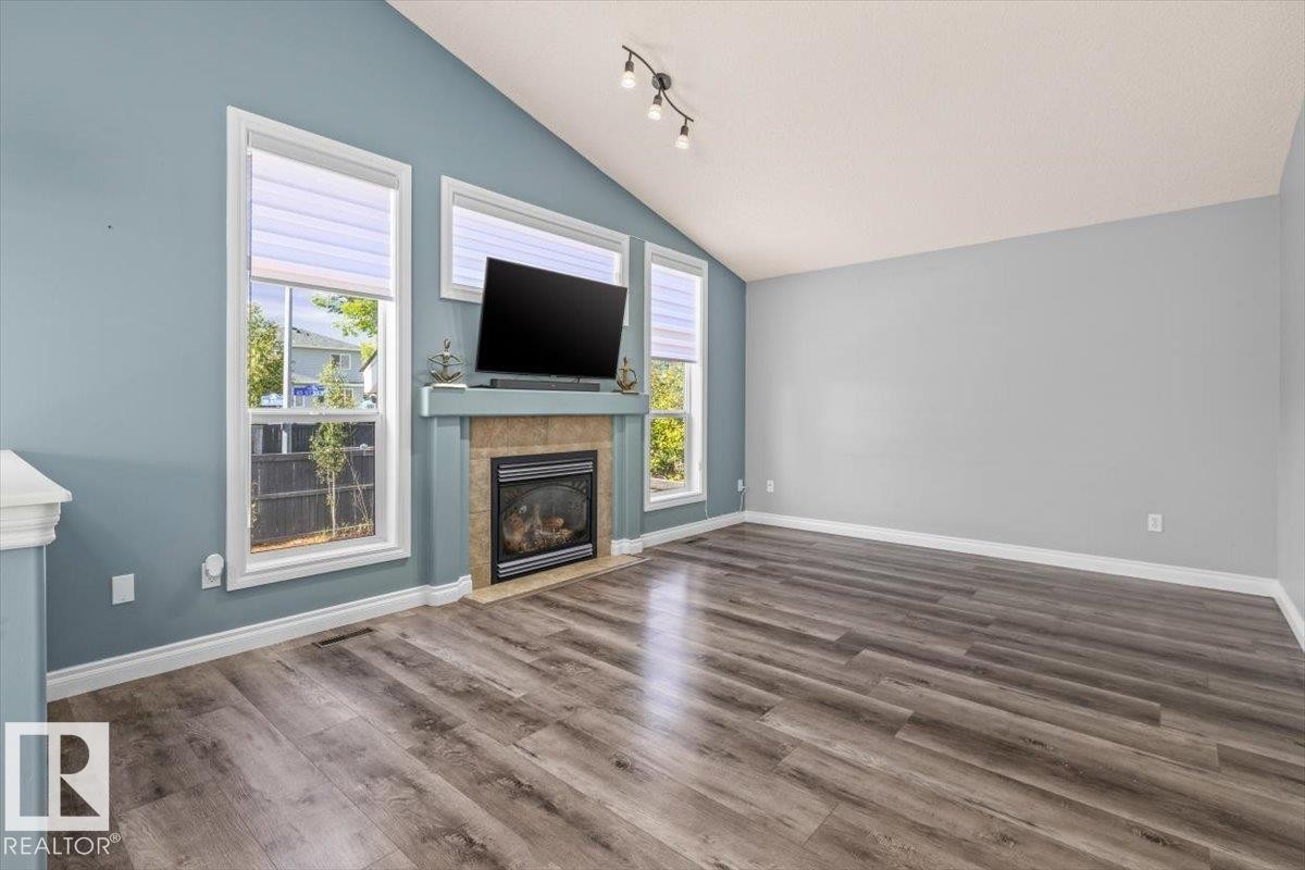 Vaulted ceiling with track lighting, wood-finish flooring, and a fireplace with a stone surround - 15420 44 Street Nw, Edmonton, AB