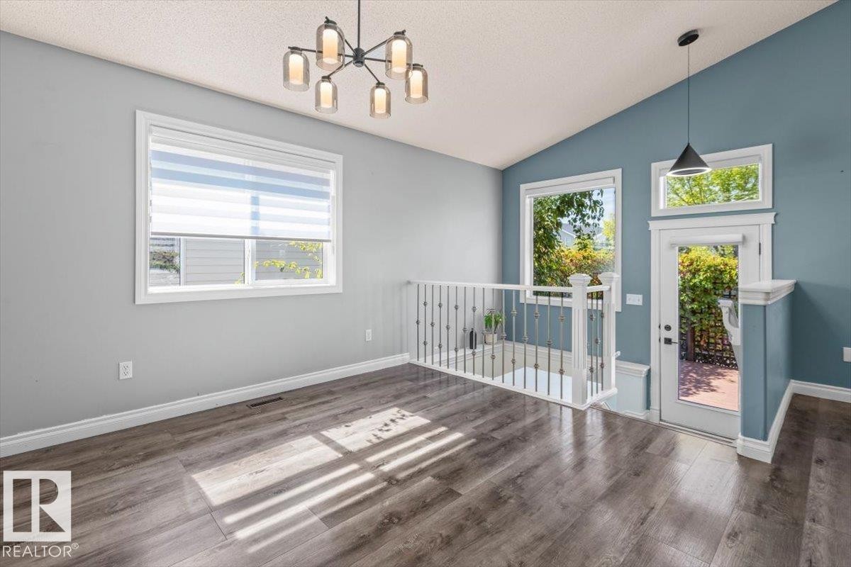 Vaulted ceiling, wood-finish flooring, contemporary chandelier, white railings, and an exterior door with transom window - 15420 44 Street Nw, Edmonton, AB