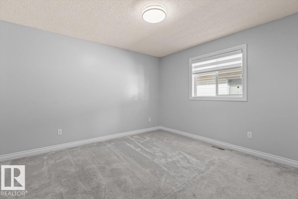 Neutral-toned walls, textured ceiling, window with blinds, and light-toned carpeting - 15420 44 Street Nw, Edmonton, AB