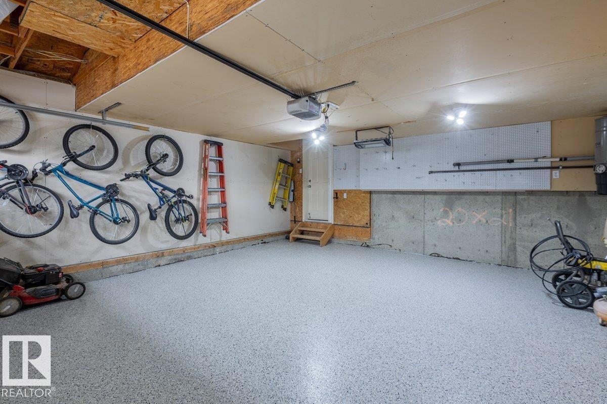 Attached garage featuring a durable epoxy floor finish, exposed wood ceiling joists, and overhead lighting - 15420 44 Street Nw, Edmonton, AB