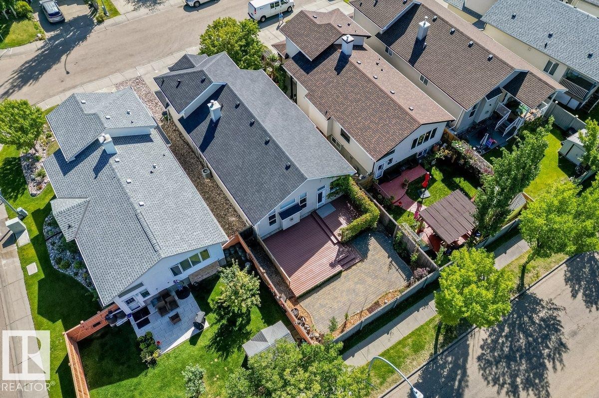 Rear yard featuring a wood-finish deck, paved patio area, and mature perimeter trees - 15420 44 Street Nw, Edmonton, AB