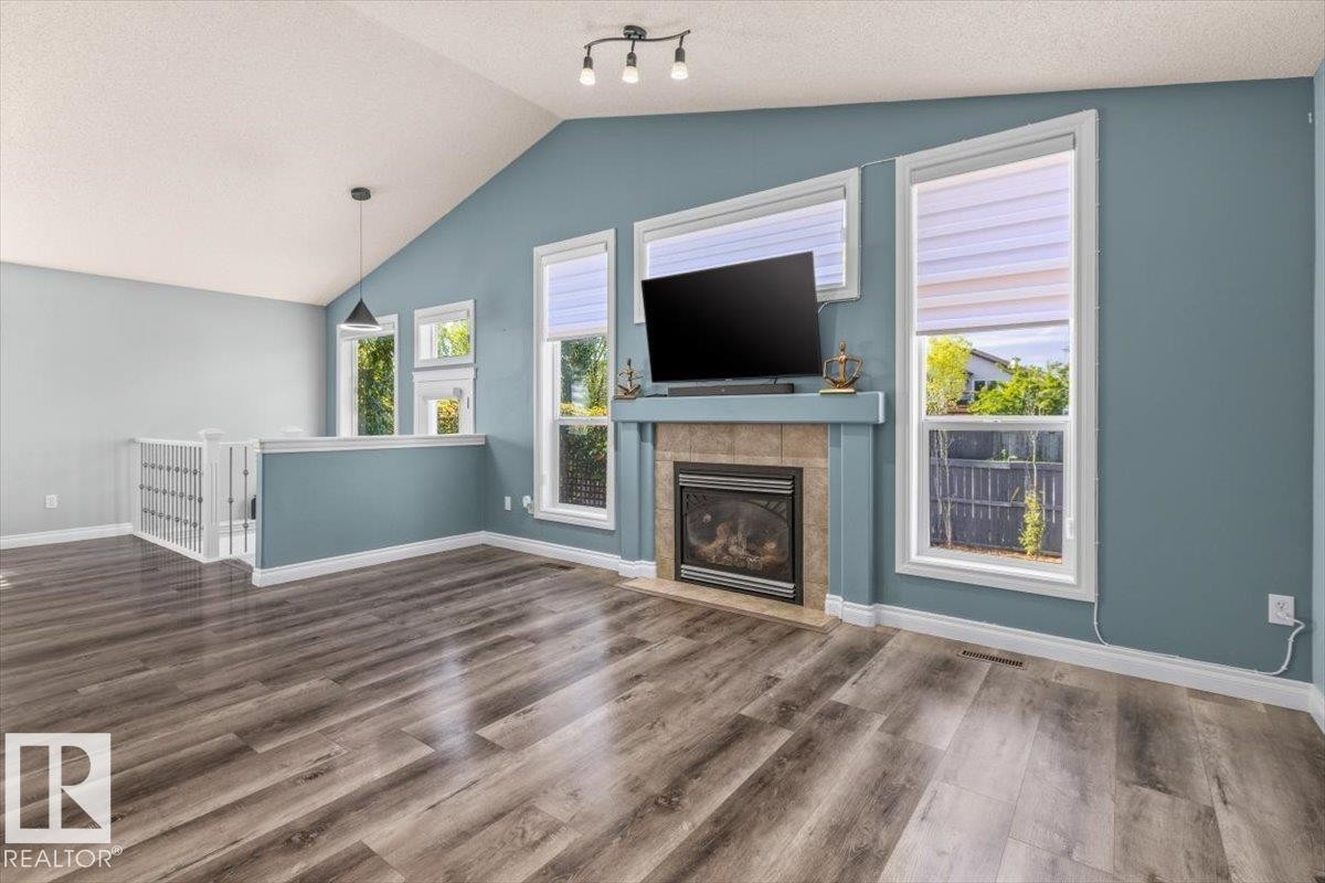 Vaulted ceiling, wood-finish flooring, fireplace with tile surround, white window trim, and white railing with balusters - 15420 44 Street Nw, Edmonton, AB