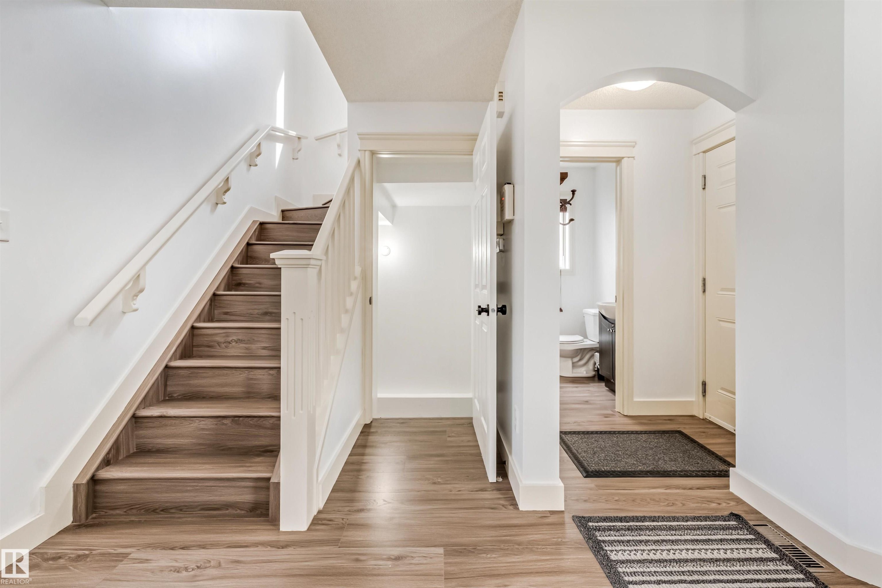 Wood-finish flooring, staircase with white railing and risers, white walls, and arched doorway - 20324 48 Avenue Nw, Edmonton, AB
