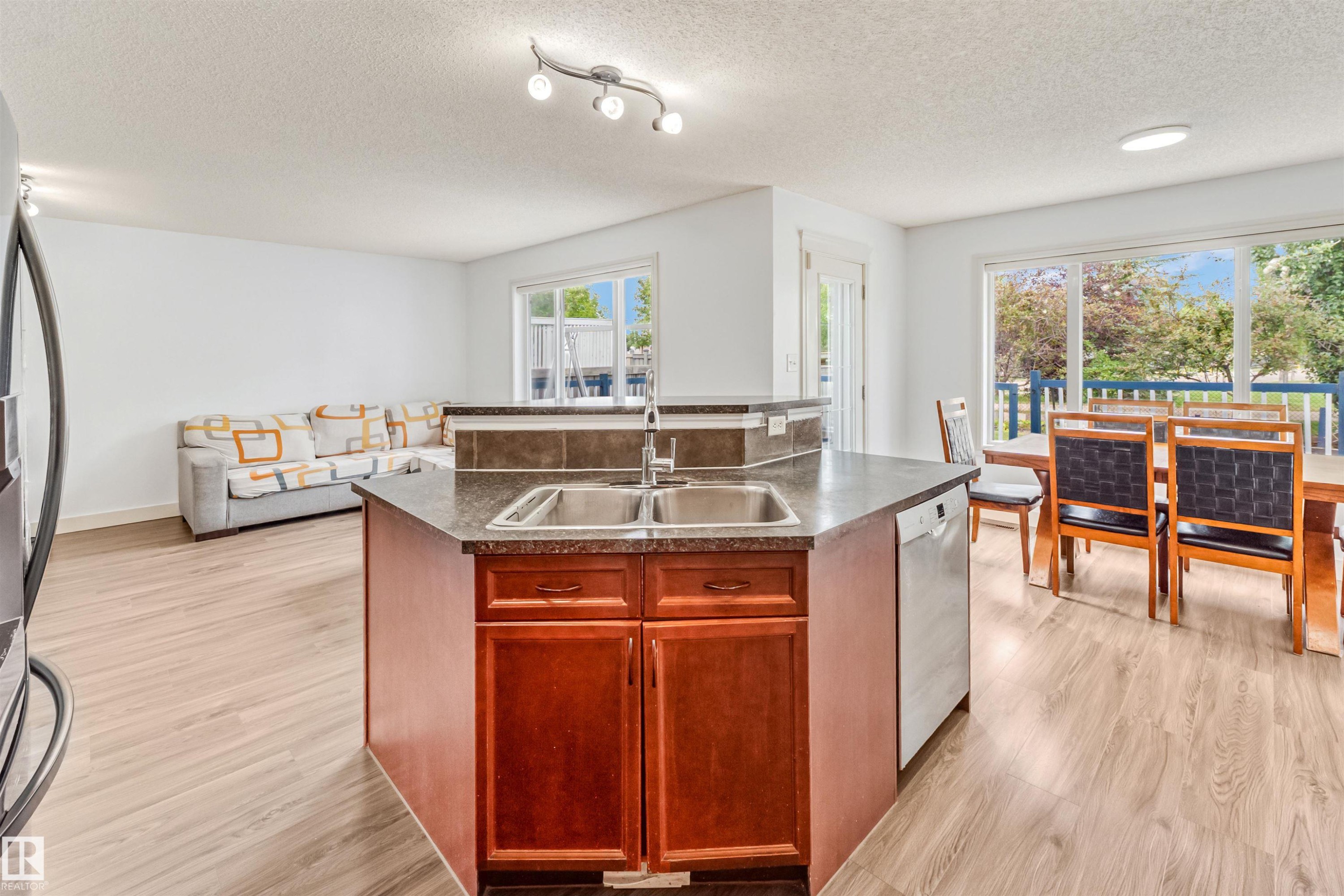 Kitchen island with dual stainless steel sink, wood-finish cabinetry, and stone-finish countertop - 20324 48 Avenue Nw, Edmonton, AB