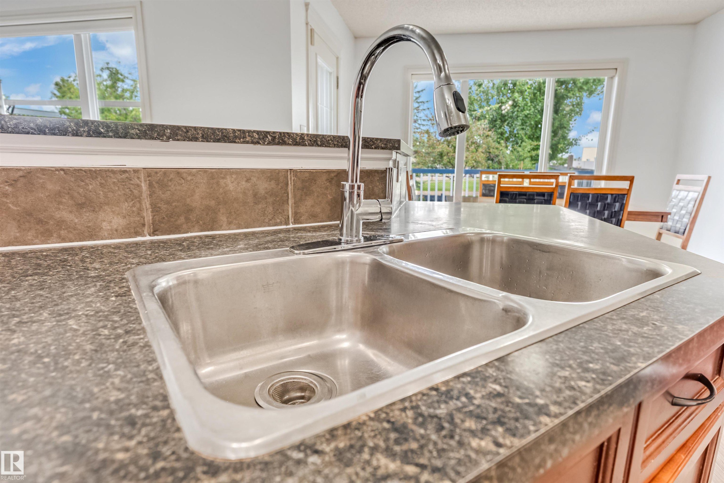 Double basin stainless steel sink with a high-arc chrome faucet, set into a speckled countertop with a tiled backsplash - 20324 48 Avenue Nw, Edmonton, AB