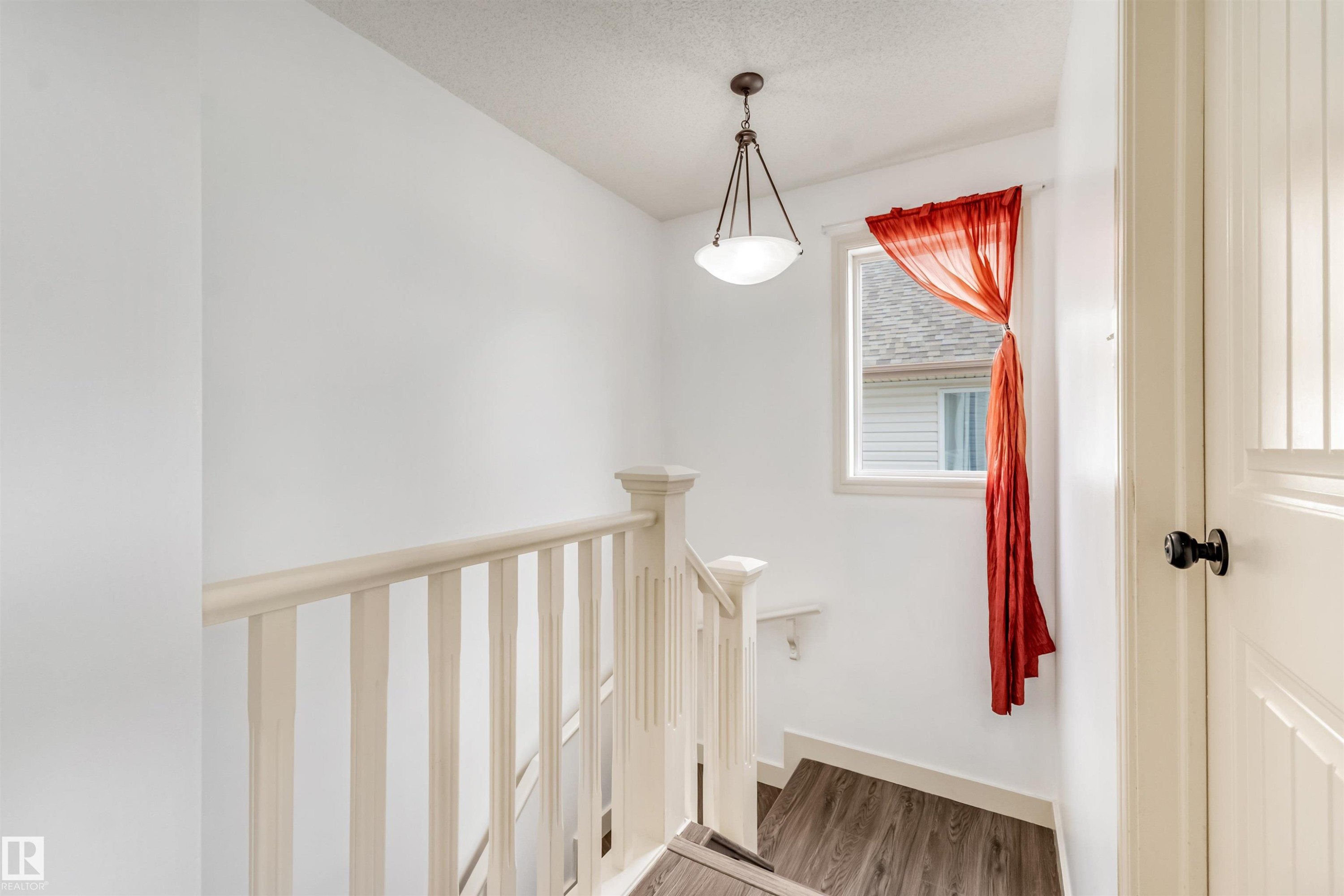 Staircase with light wood-finish flooring, white spindle railing, and a window providing natural illumination - 20324 48 Avenue Nw, Edmonton, AB