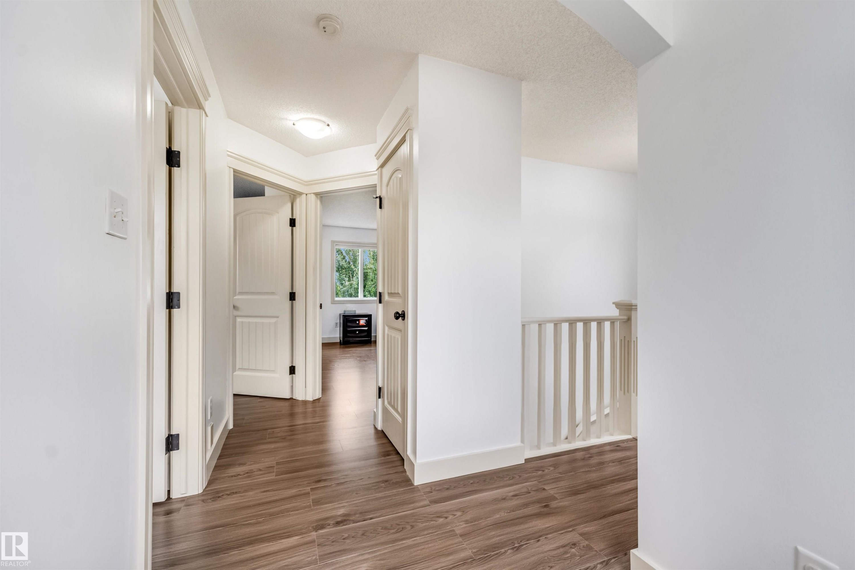 Wood-finish flooring throughout, white interior doors with dark hardware, bright white walls, and a visible stair railing - 20324 48 Avenue Nw, Edmonton, AB