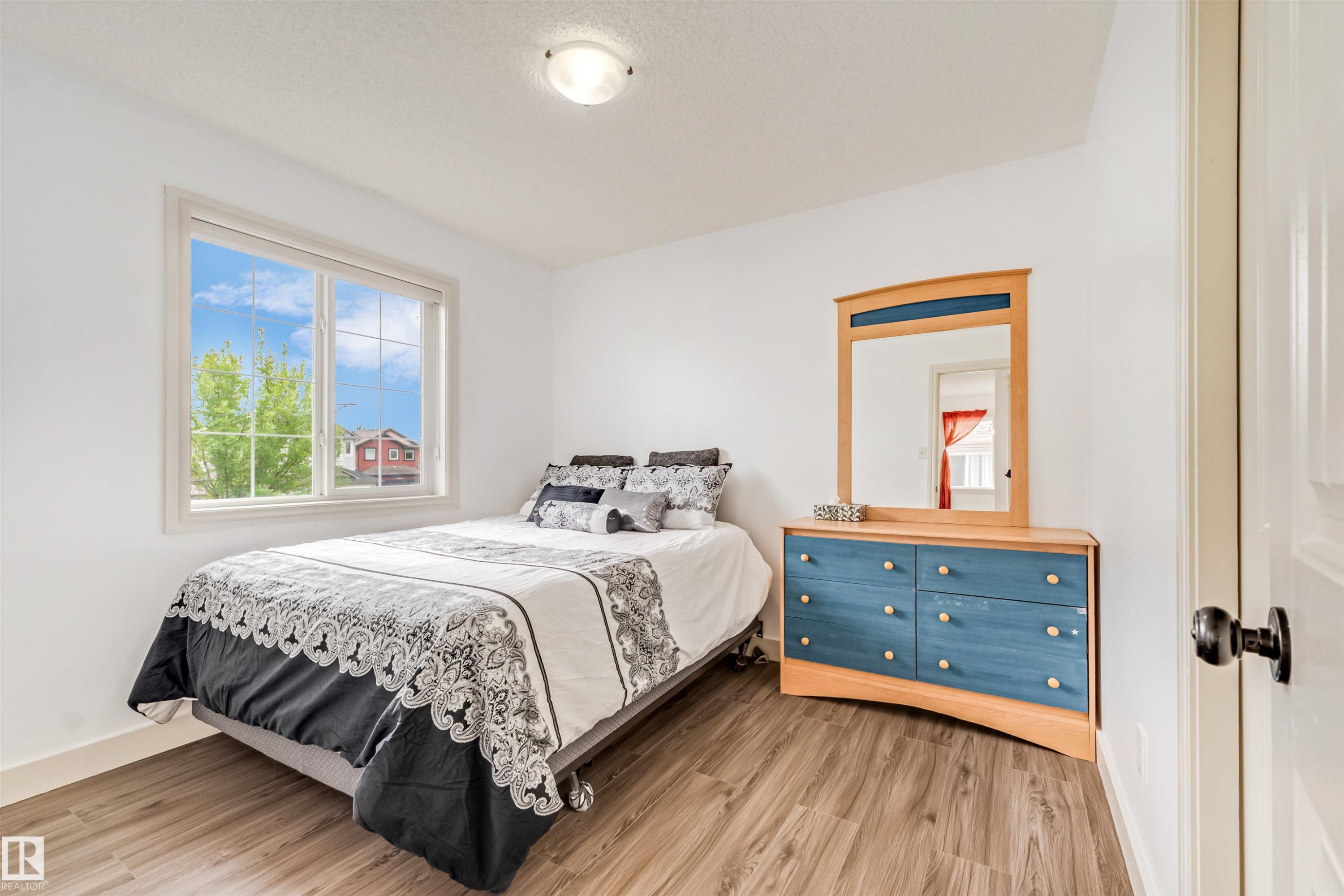 Bright room with a large window, wood-finish flooring, white walls, and a ceiling-mounted light fixture - 20324 48 Avenue Nw, Edmonton, AB