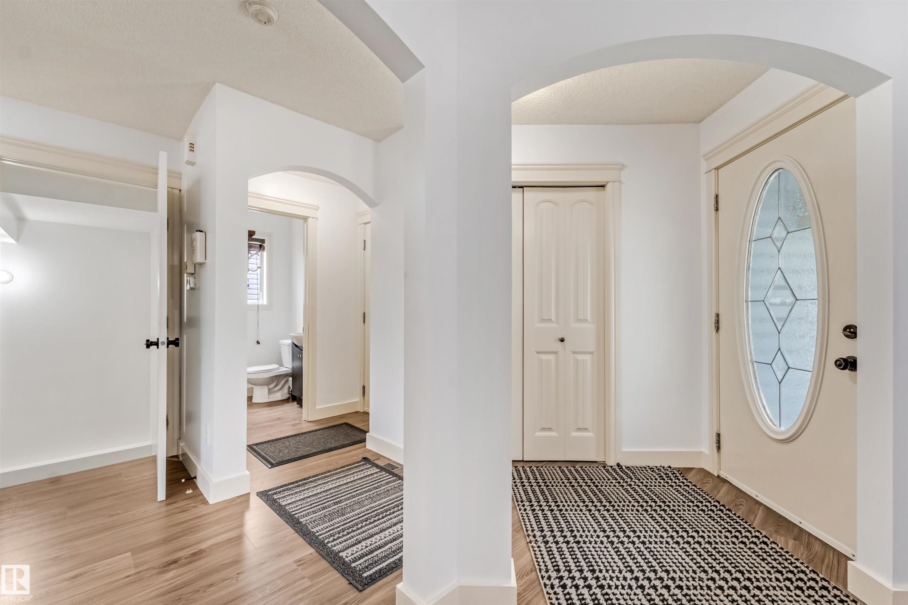 Entryway featuring wood-finish flooring, an arched doorway, and a front door with decorative glass - 20324 48 Avenue Nw, Edmonton, AB