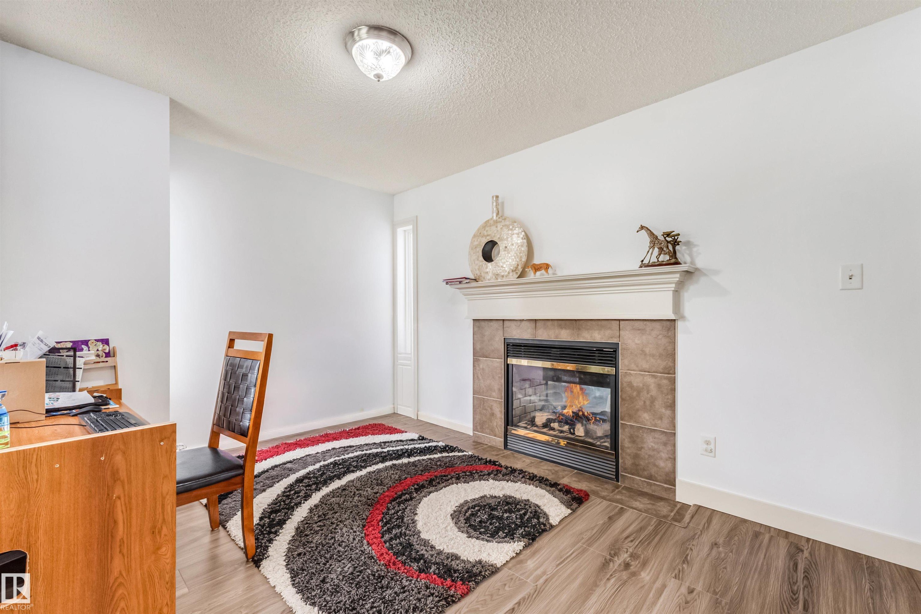 White walls and wood-finish flooring complement the electric fireplace with a tiled surround and white mantel - 20324 48 Avenue Nw, Edmonton, AB