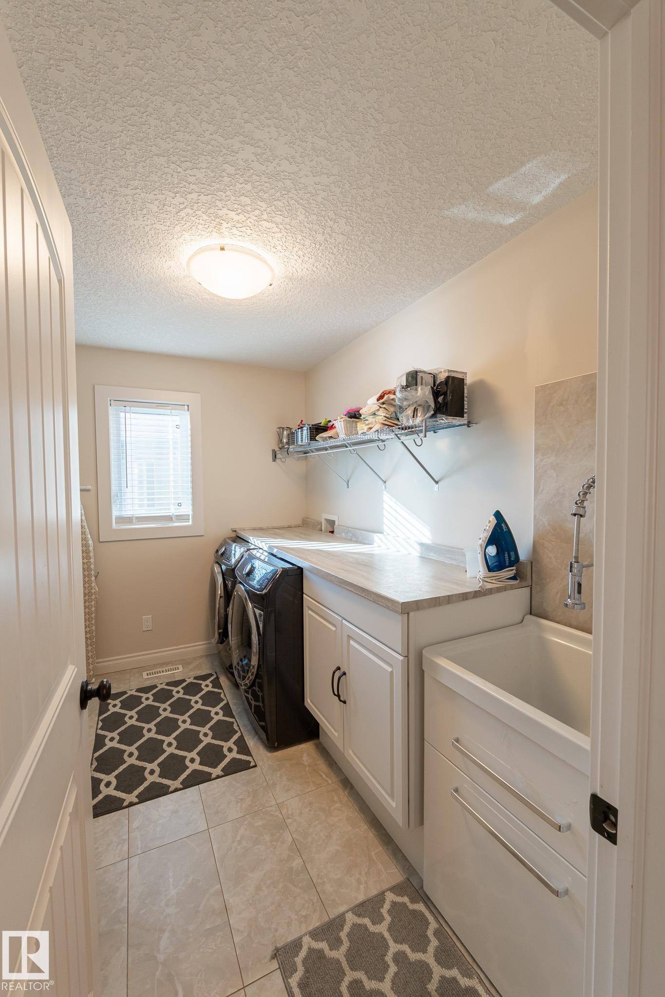 Laundry area featuring a utility sink, white cabinetry, a countertop, tiled flooring, and a window - 914 Crystallina Nera Way Nw, Edmonton, AB