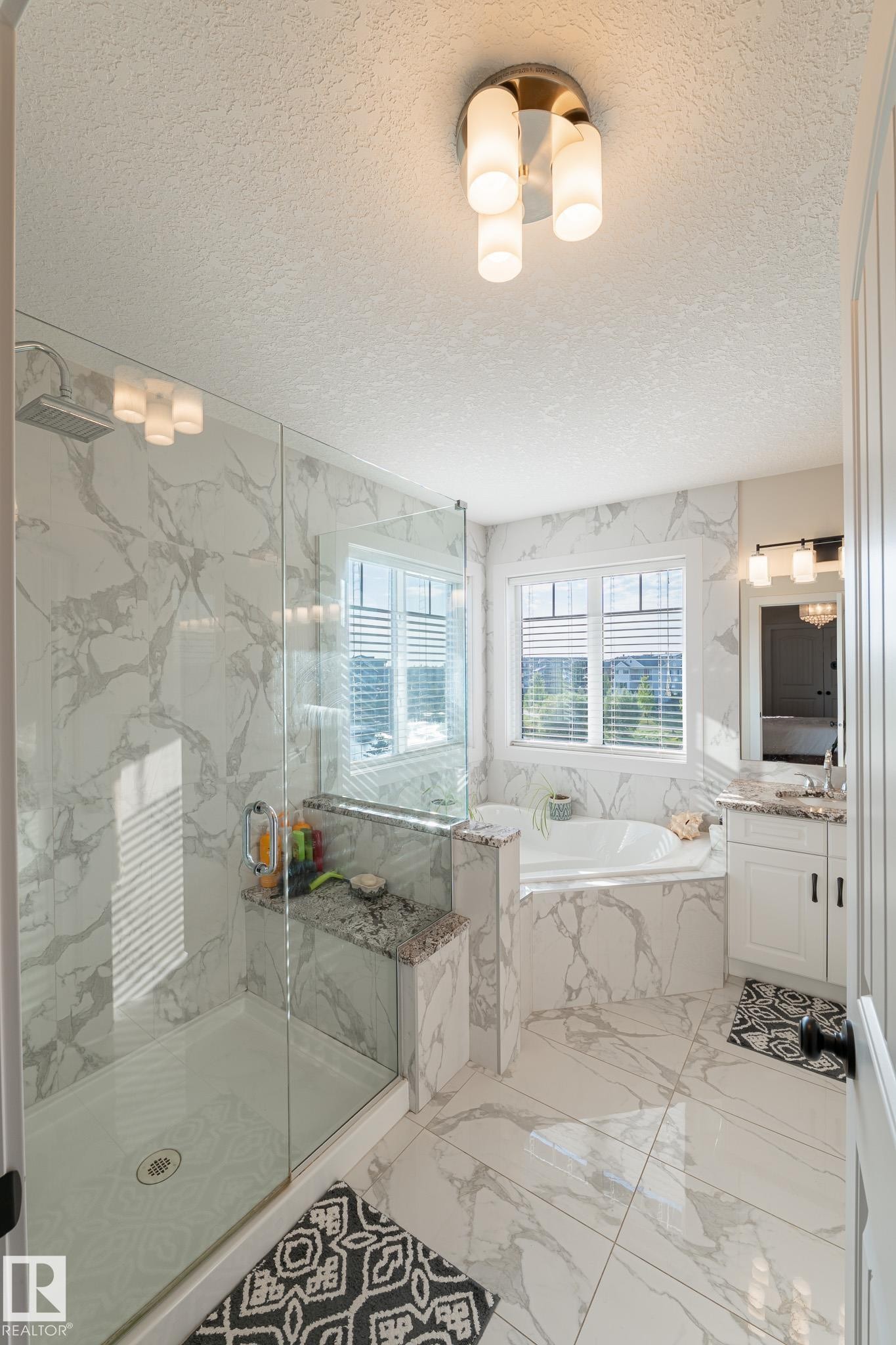 Enclosed shower with glass panel, built-in bench with stone top, and large format wall and floor tiling - 914 Crystallina Nera Way Nw, Edmonton, AB