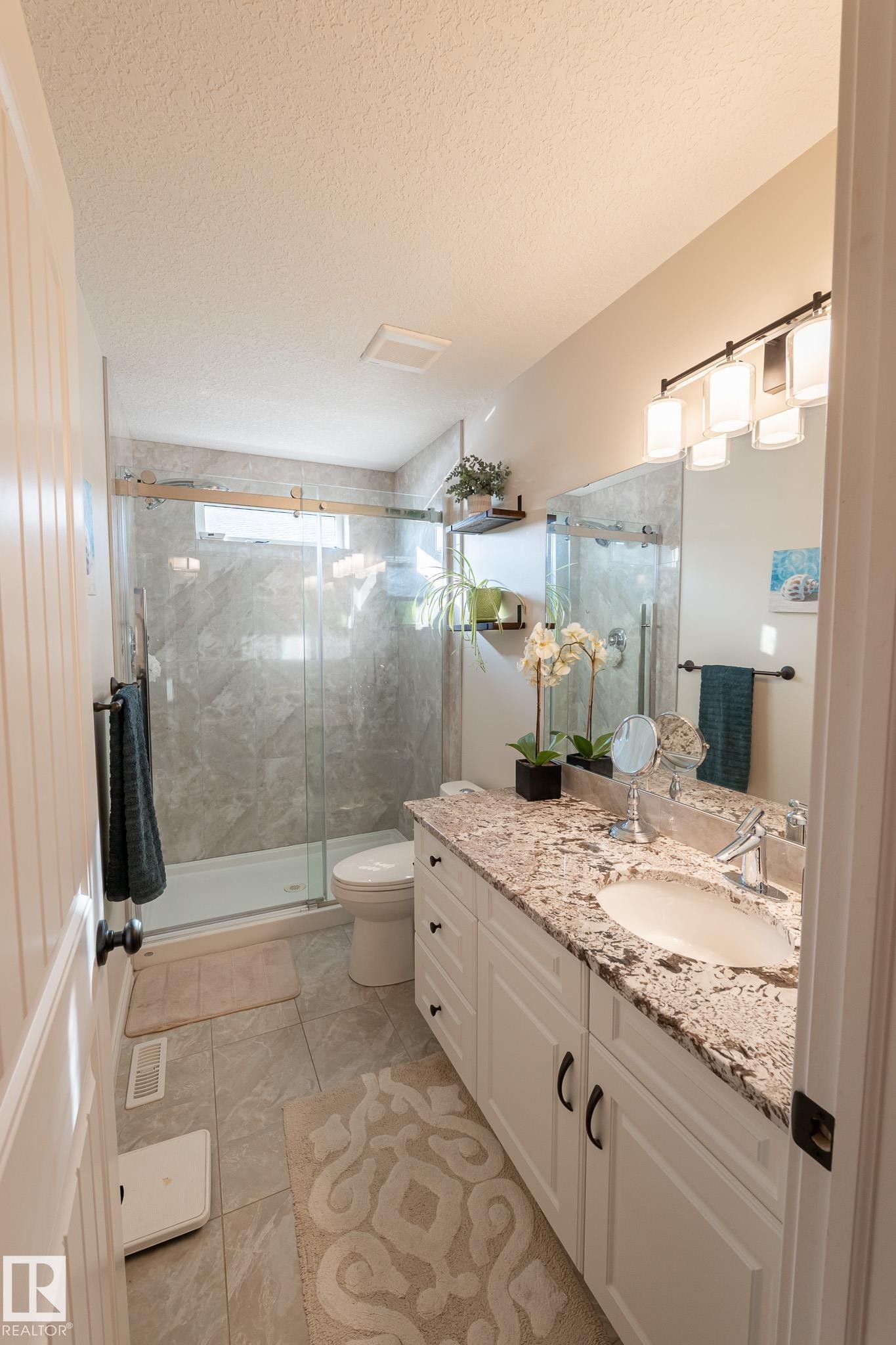 Dual-sink vanity with a granite countertop, white cabinetry, and matte black hardware - 914 Crystallina Nera Way Nw, Edmonton, AB