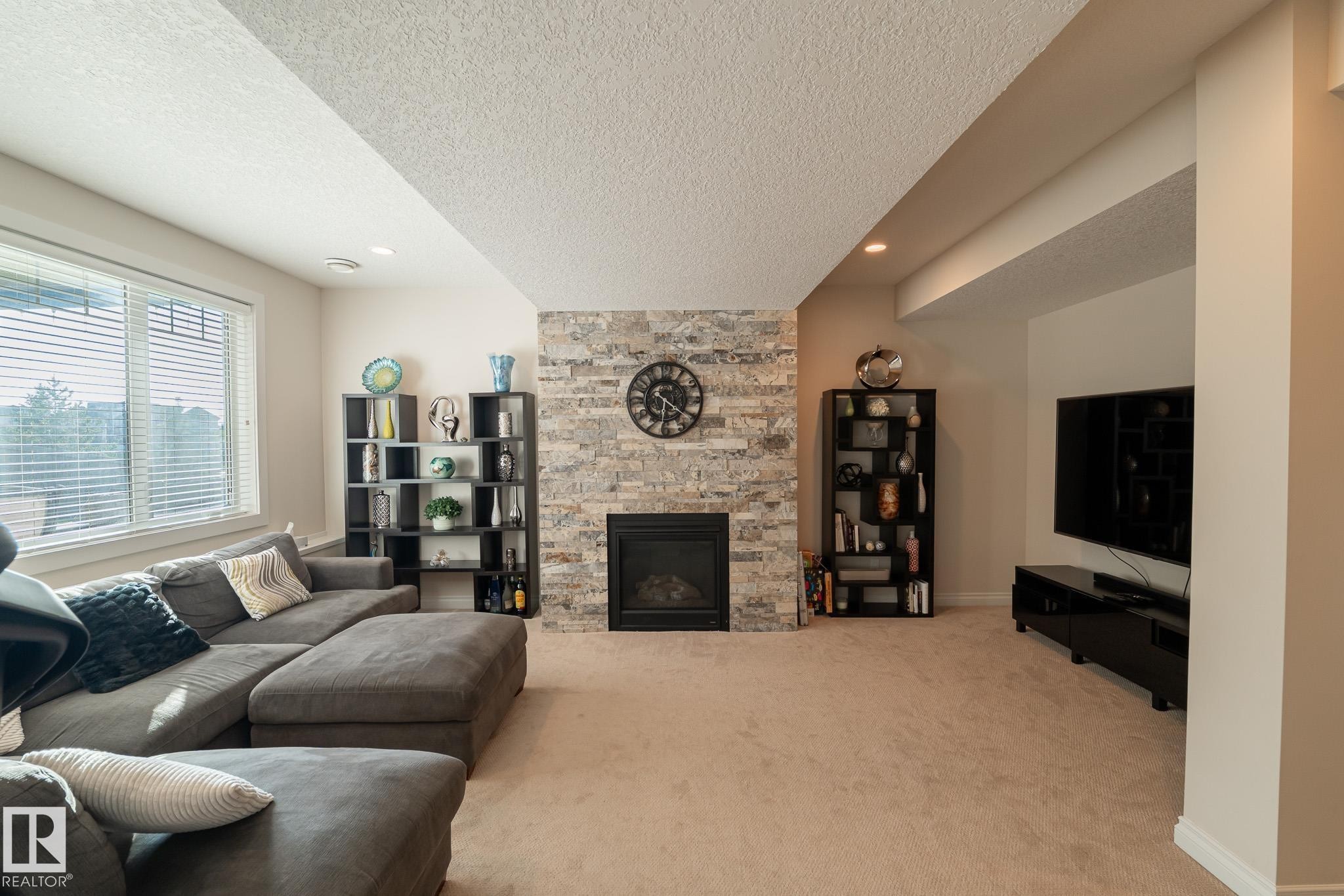 Fireplace with stone surround, recessed lighting, large window with blinds, and carpeted flooring - 914 Crystallina Nera Way Nw, Edmonton, AB