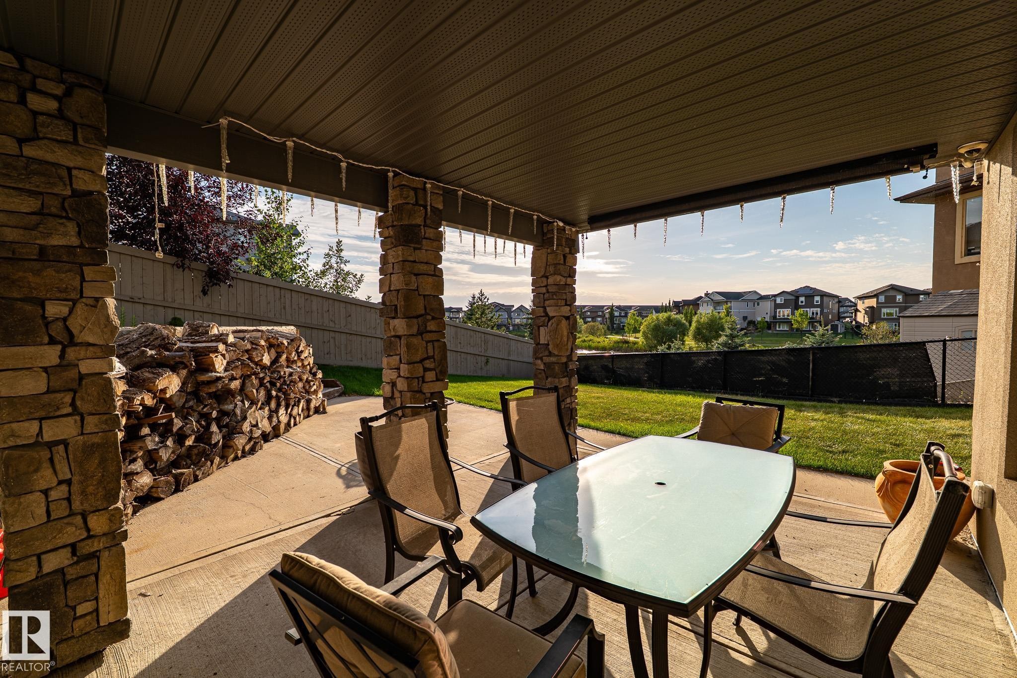 Covered patio with stone-clad columns, concrete flooring, and an expansive lawn area - 914 Crystallina Nera Way Nw, Edmonton, AB