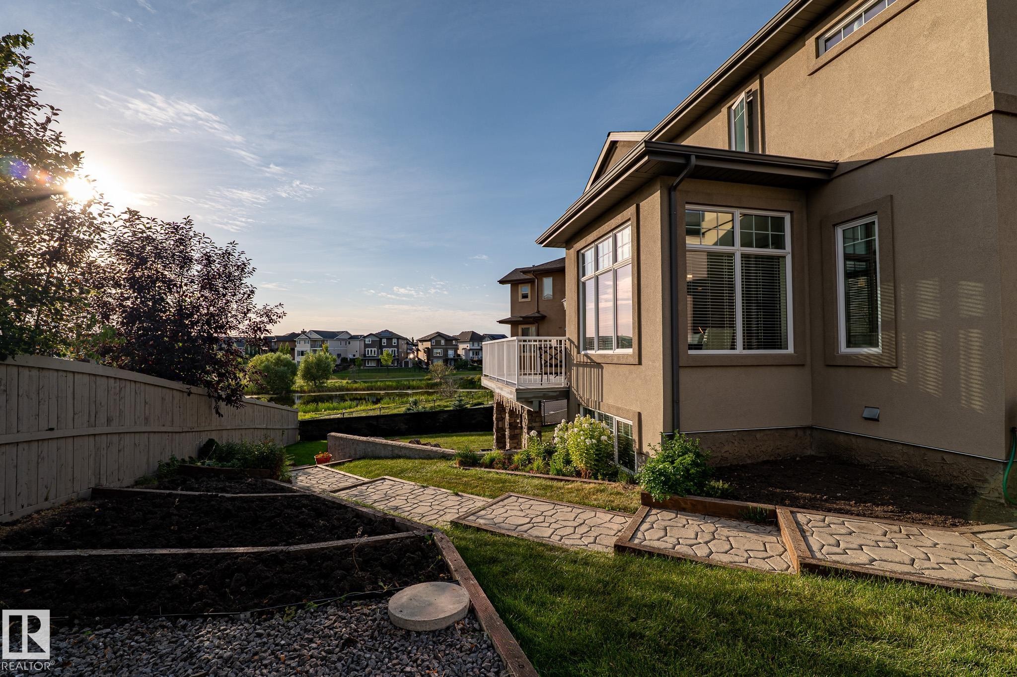 Exterior featuring stucco siding, multiple windows with white trim, a balcony with white railings, a landscaped yard with a pathway, and terraced garden beds - 914 Crystallina Nera Way Nw, Edmonton, AB