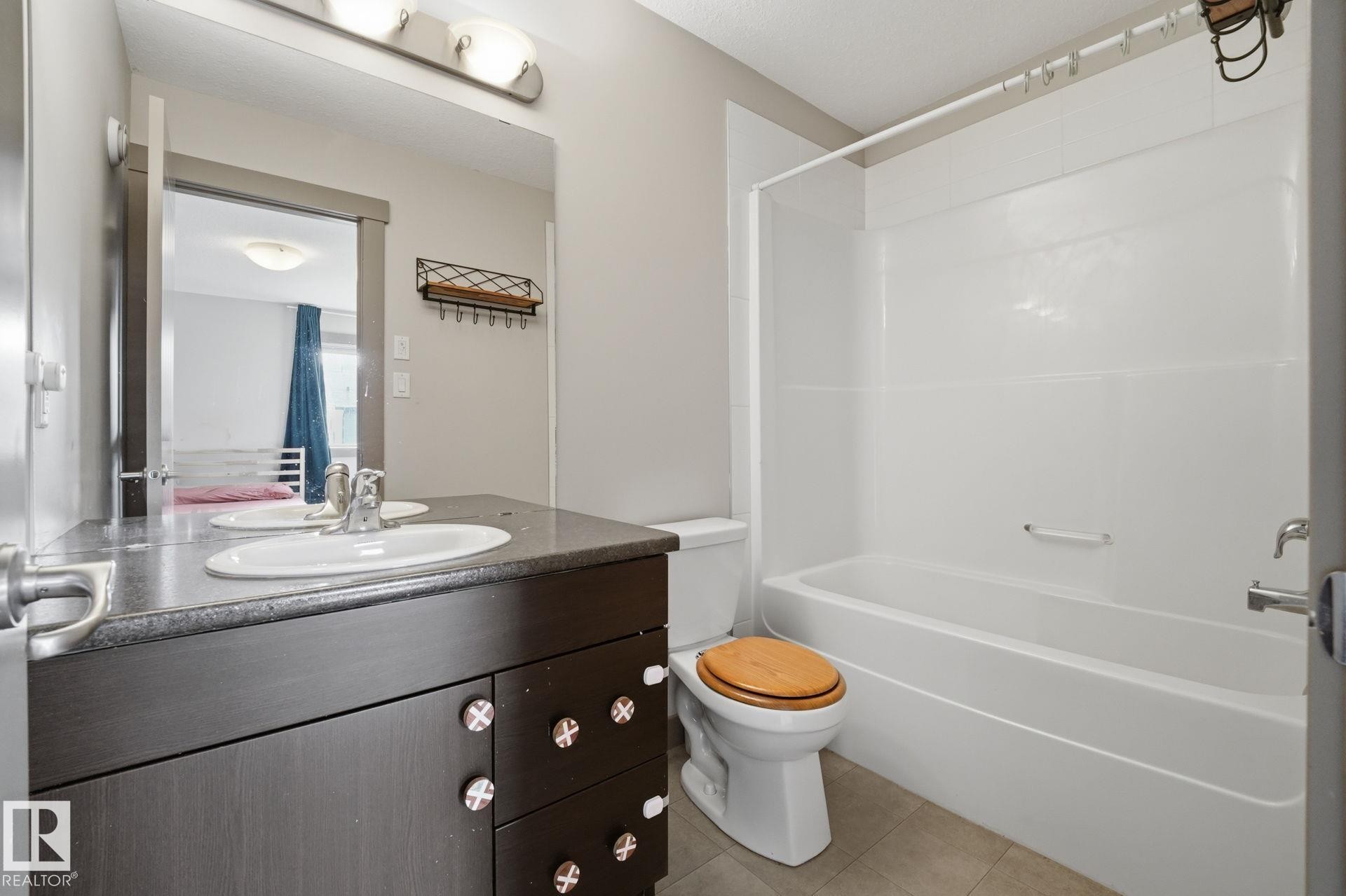 Master bathroom featuring a single vanity with a dark wood-finish cabinet and stone-look countertop, a white sink with a chrome faucet, and a combination tub and shower with white surround panels - 17621 10 Avenue Sw, Edmonton, AB - Indoor Photo Showing Bathroom