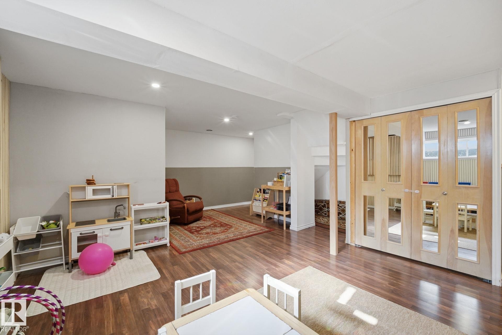 Spacious finished lower level featuring wood-finish flooring, recessed lighting, a two-tone wall treatment, and light wood bi-fold doors hiding the laundry - 17621 10 Avenue Sw, Edmonton, AB - Indoor