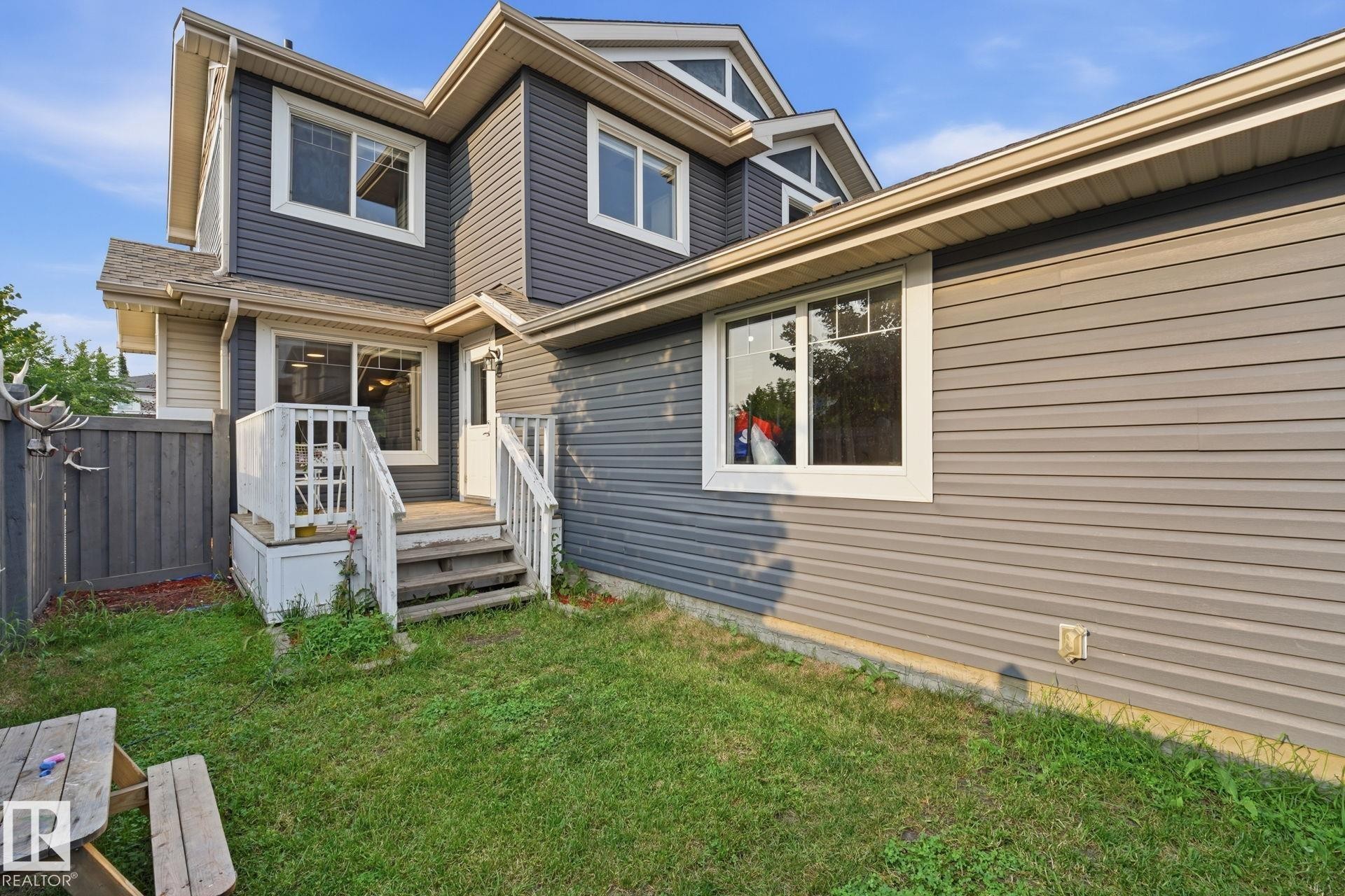 Multi-level rear exterior with gray siding, white trim windows, and a raised deck with steps - 17621 10 Avenue Sw, Edmonton, AB - Outdoor