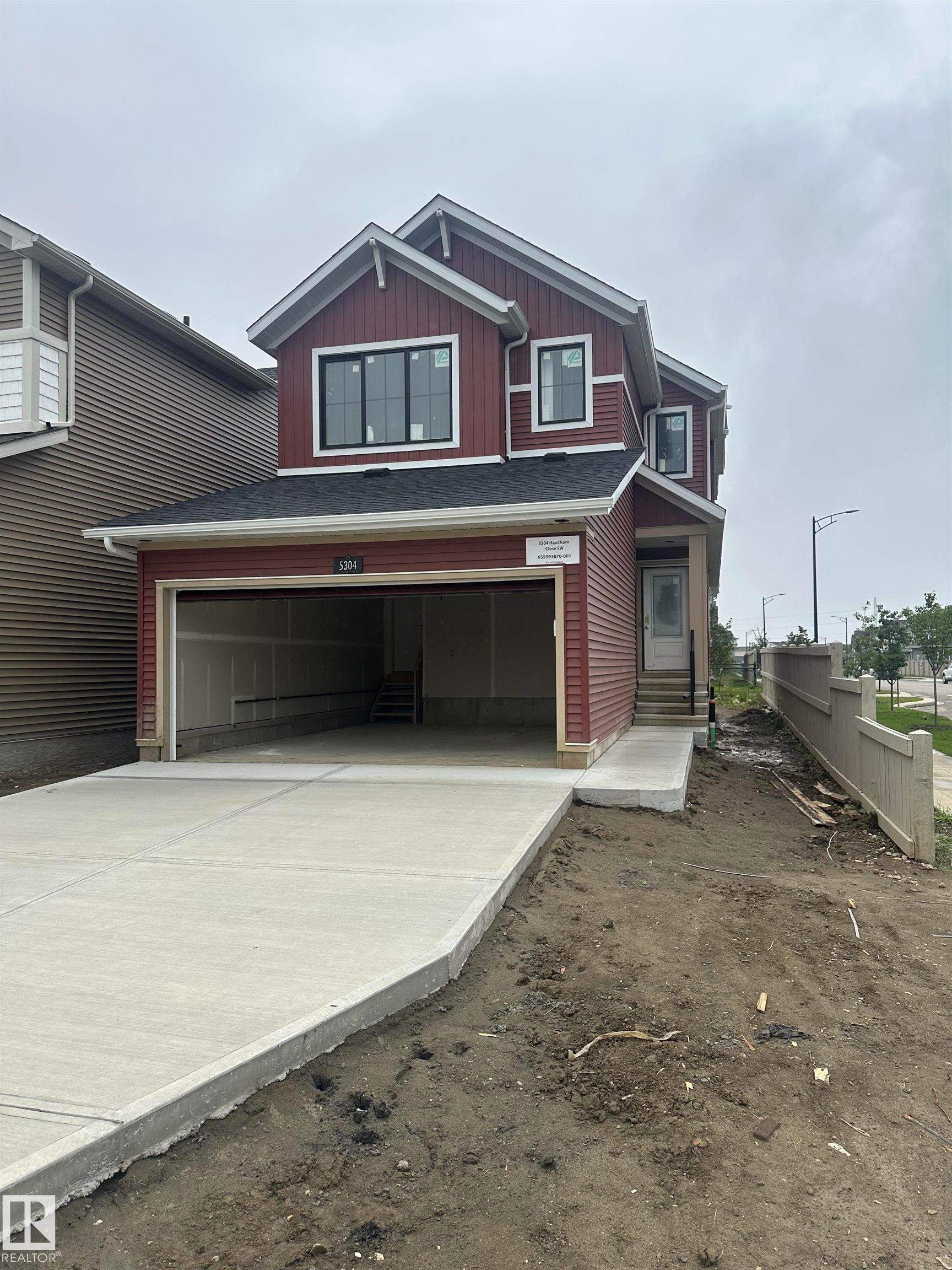 Two-story exterior with red siding, attached garage, concrete driveway, and front entry - 5304 Hawthorn Close Sw, Edmonton, AB