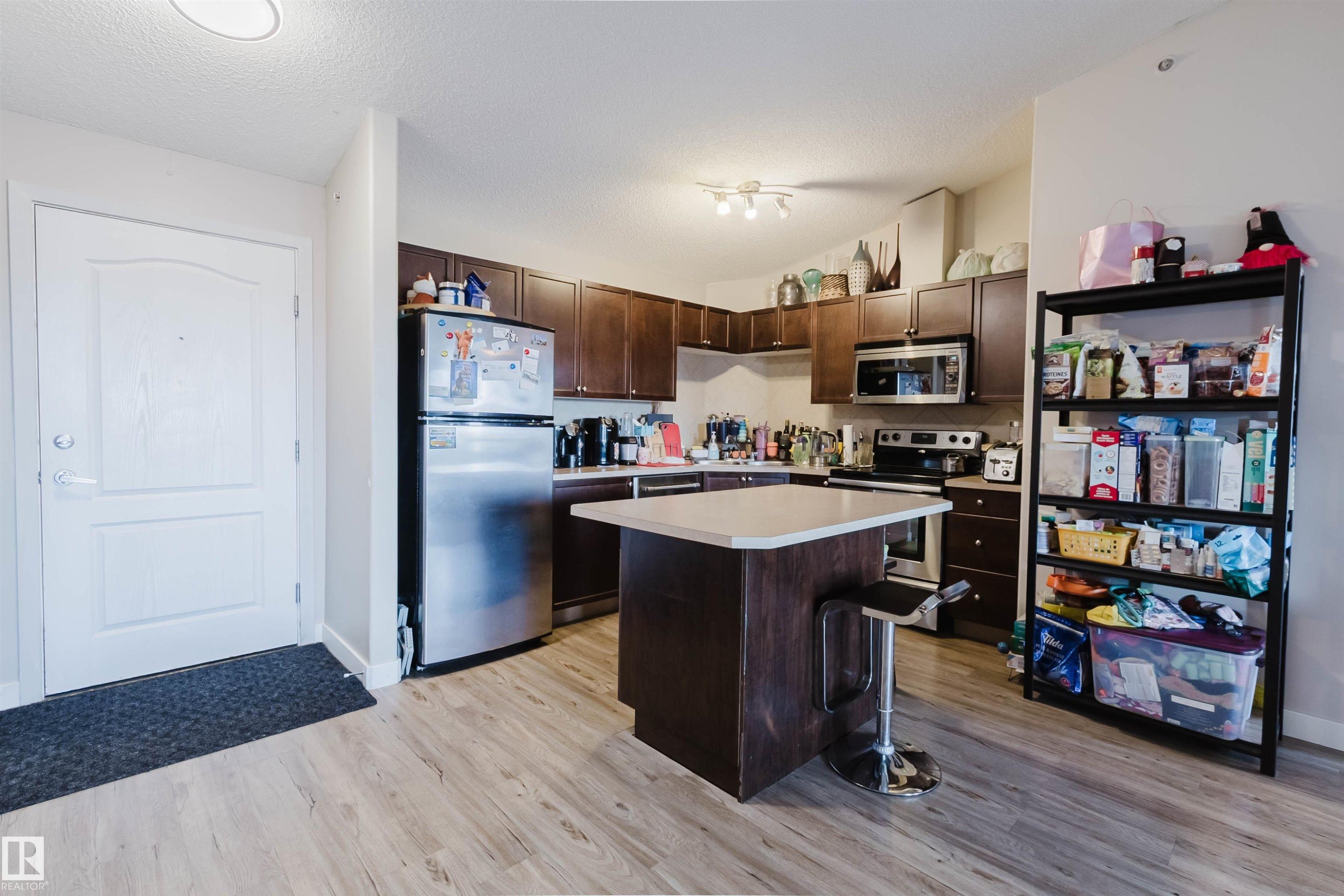 Kitchen featuring wood-finish flooring, dark wood cabinetry, stainless steel appliances, and a central island with a light-colored countertop - #7428 7327 South Terwillegar Dr Nw, Edmonton, AB