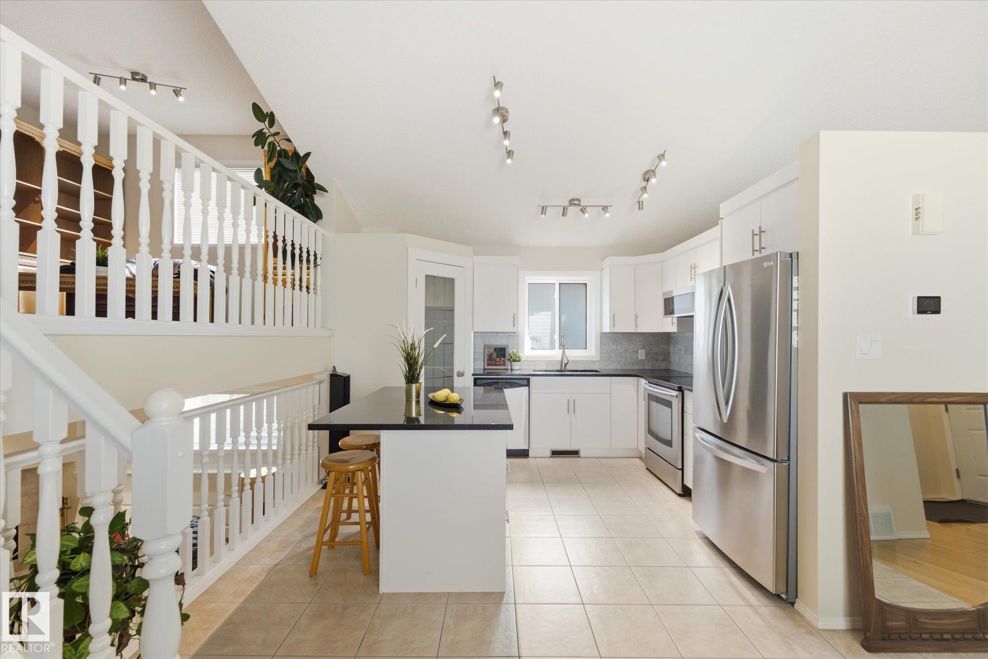 Kitchen featuring white cabinetry, stainless steel appliances, a black countertop island, and tile flooring - 1709 Turvey Bend Bend Nw, Edmonton, AB