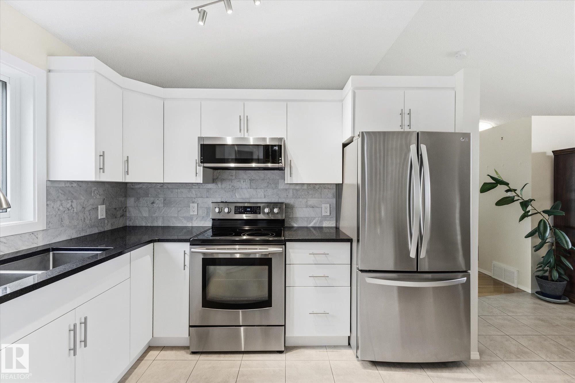 White cabinetry with brushed nickel hardware, stainless steel appliances, dark stone countertops, and a gray tile backsplash - 1709 Turvey Bend Bend Nw, Edmonton, AB