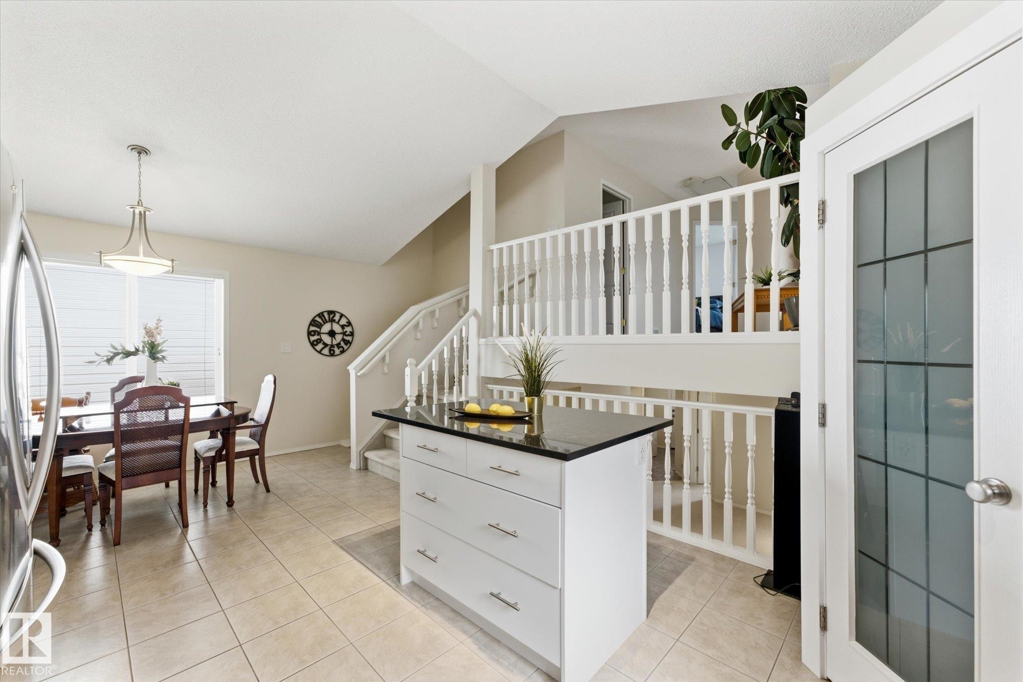Kitchen island with dark countertop, tiled flooring, built-in staircase, and frosted glass door - 1709 Turvey Bend Bend Nw, Edmonton, AB