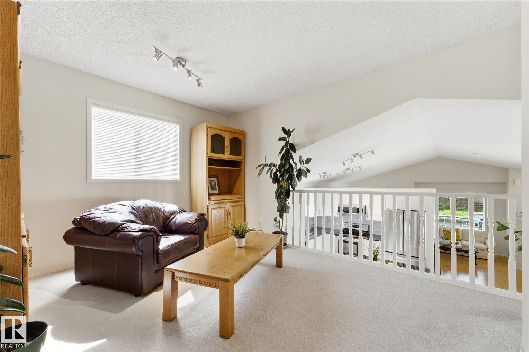 Vaulted ceiling with track lighting, white railing, built-in shelving, window with blinds, and light-colored carpeting - 1709 Turvey Bend Bend Nw, Edmonton, AB