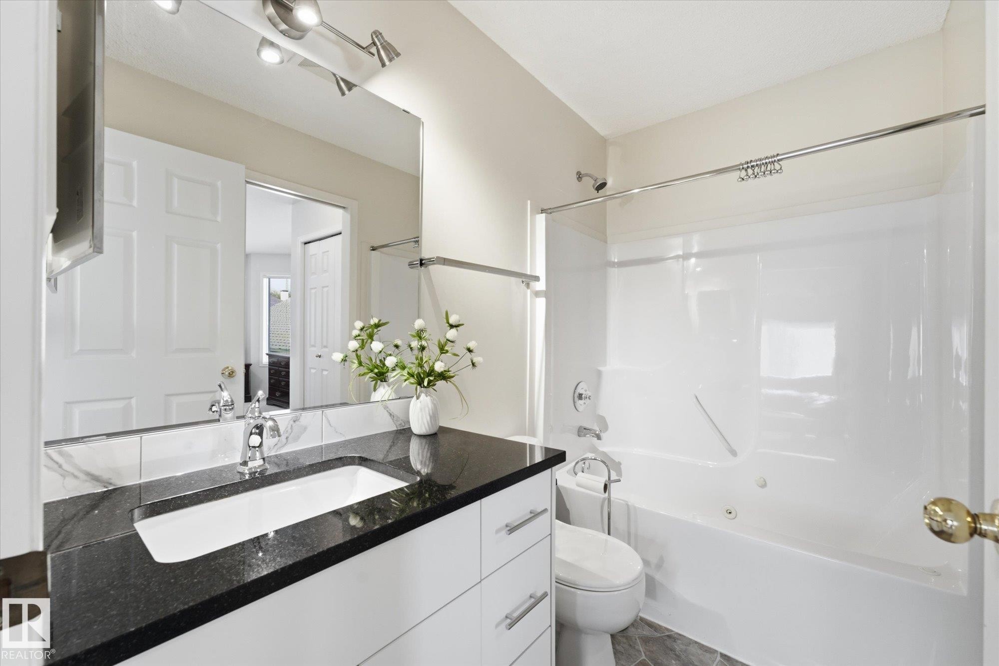 Bathroom featuring a white vanity with a dark stone countertop, undermount sink, and polished chrome faucet - 1709 Turvey Bend Bend Nw, Edmonton, AB