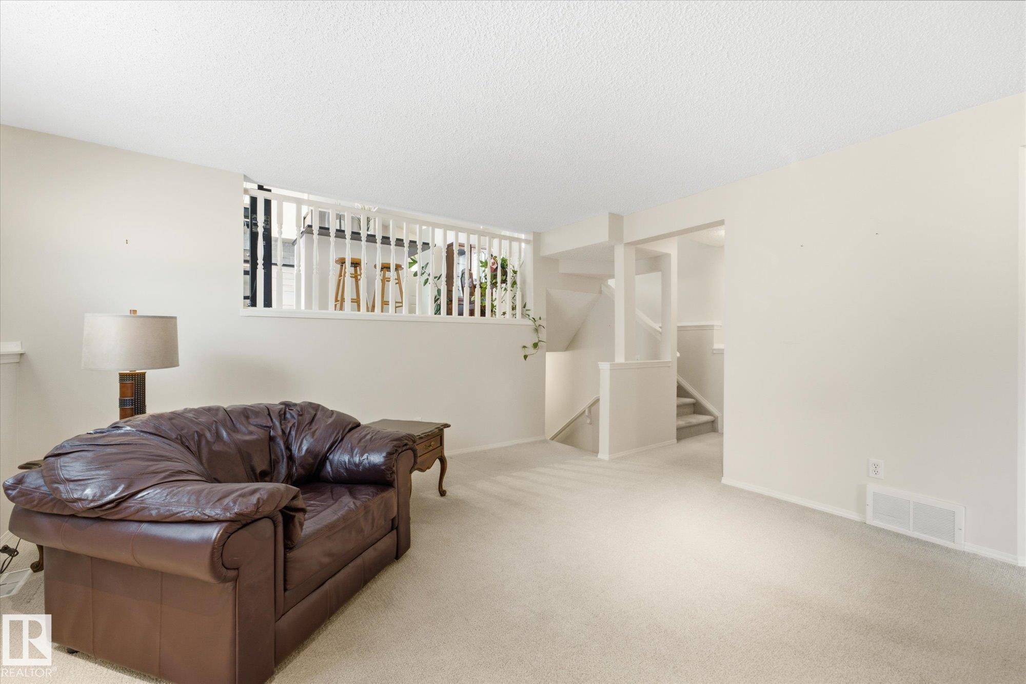 Spacious carpeted room with neutral wall tones and a built-in white baluster railing - 1709 Turvey Bend Bend Nw, Edmonton, AB