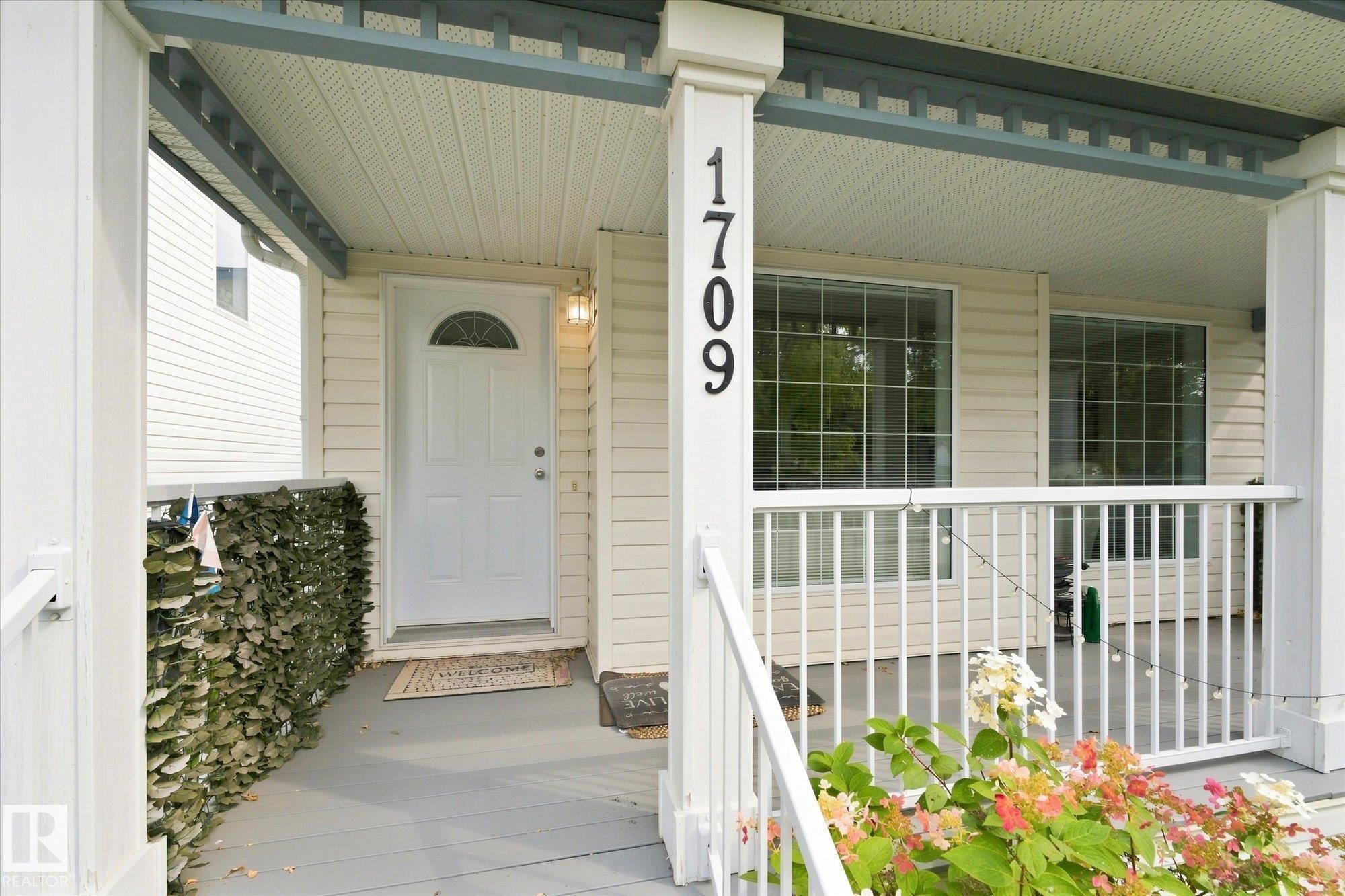 Covered front porch with white railings, a paneled entry door with an arched window, and two multi-pane windows - 1709 Turvey Bend Bend Nw, Edmonton, AB