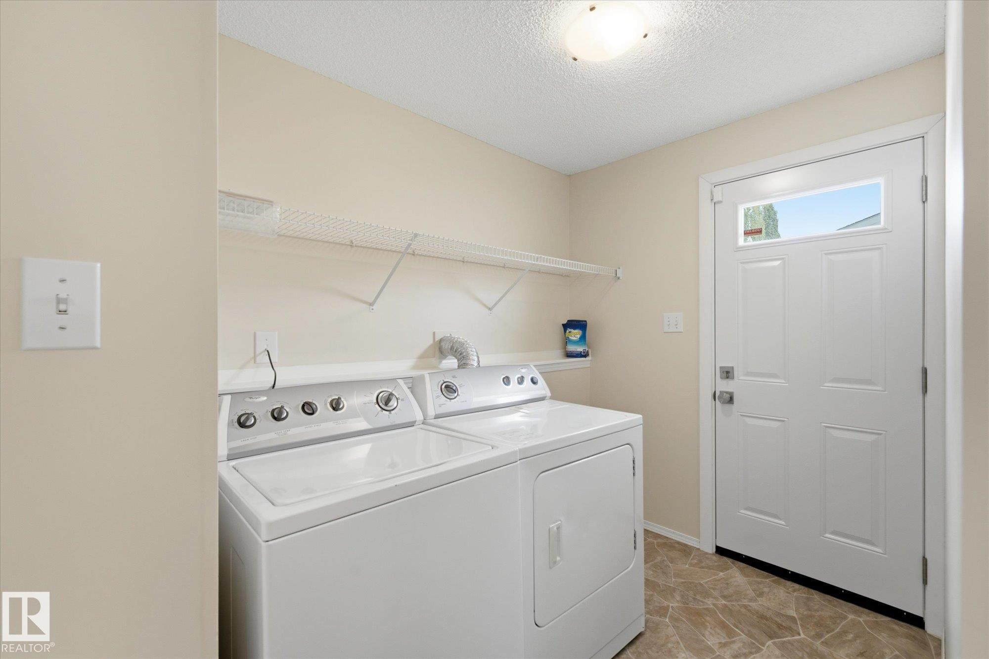 Dedicated laundry area featuring a full-light entry door, overhead shelving, and neutral wall tones - 1709 Turvey Bend Bend Nw, Edmonton, AB