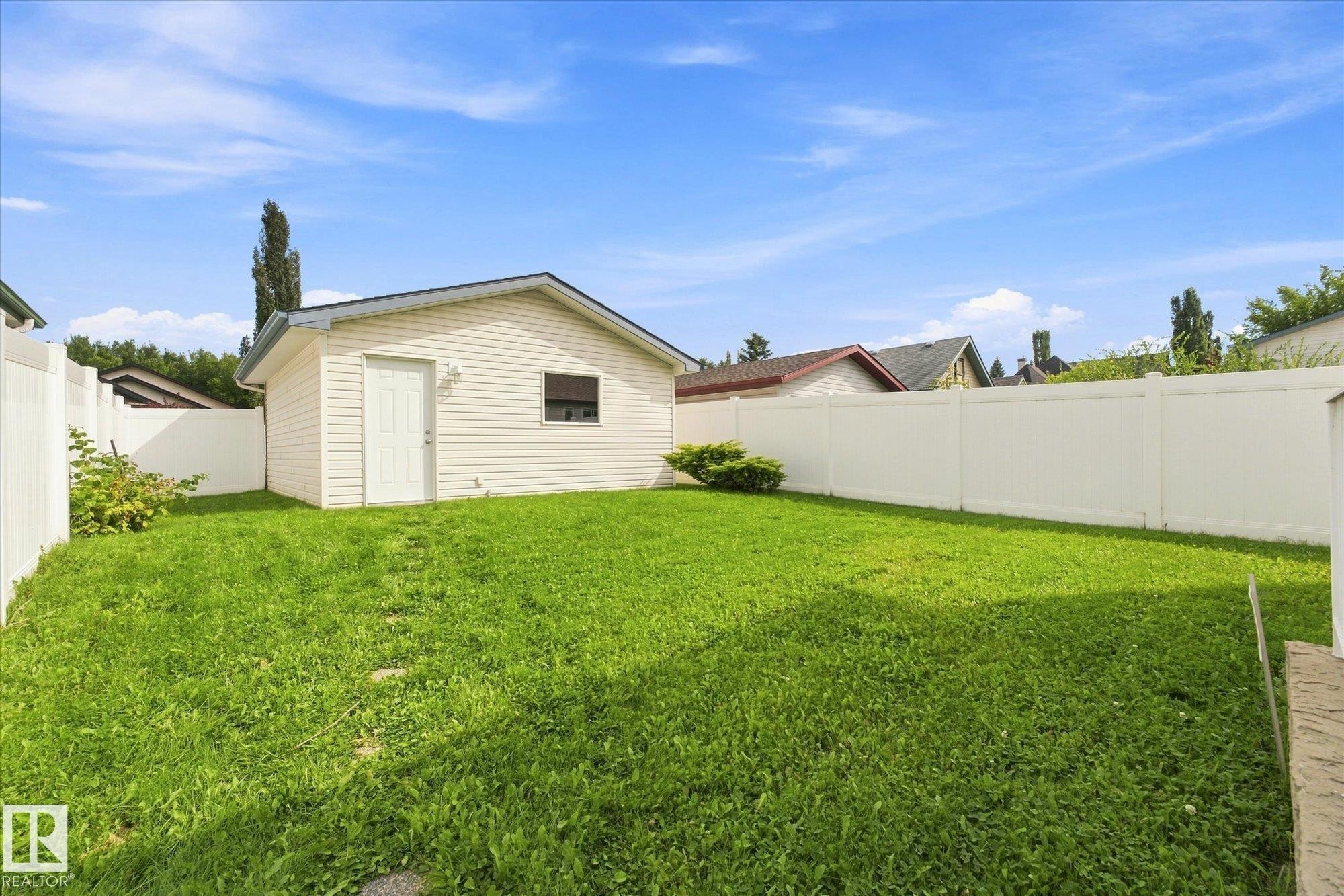Expansive backyard featuring a manicured lawn, white privacy fencing, and a detached structure with siding - 1709 Turvey Bend Bend Nw, Edmonton, AB