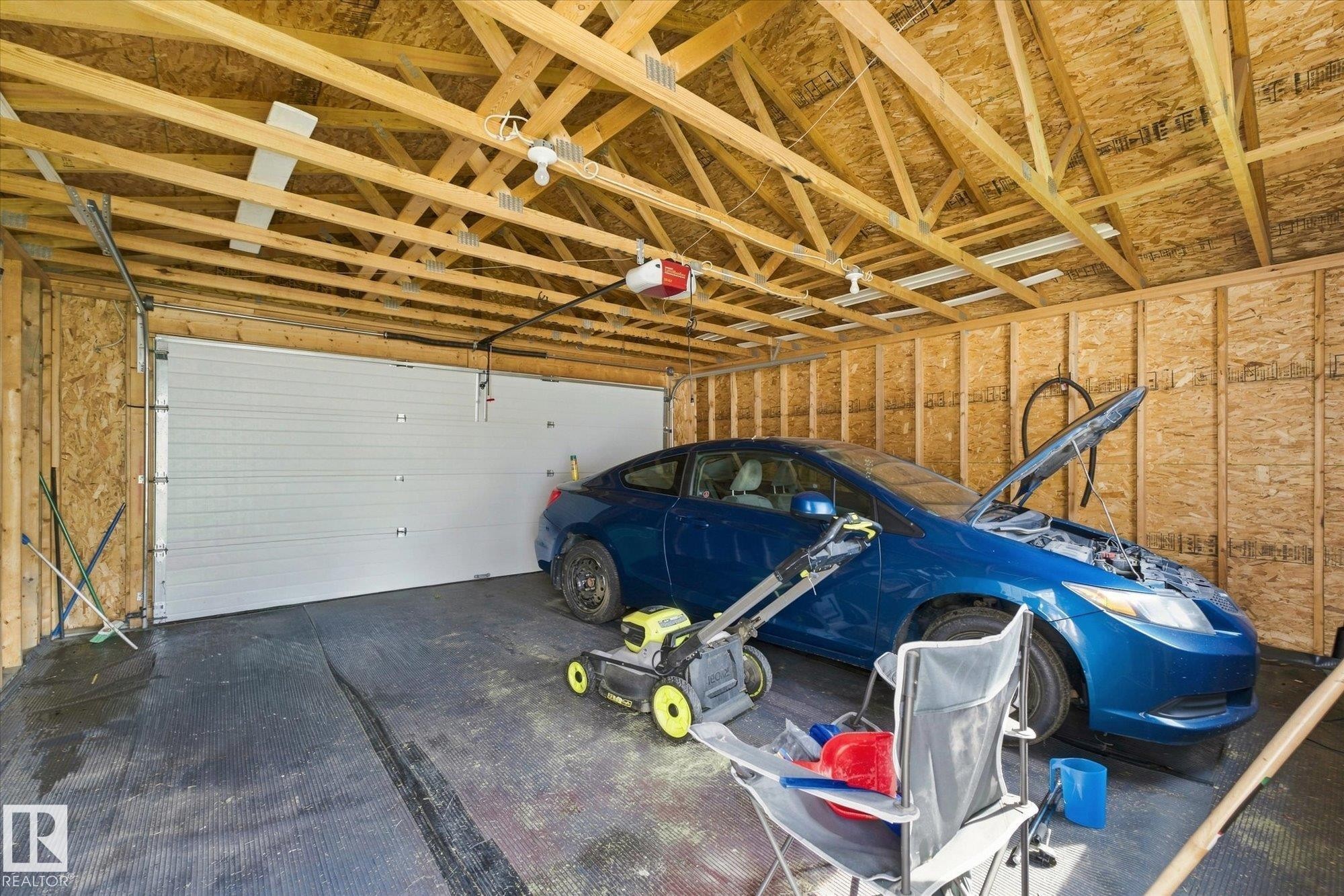 Unfinished garage space featuring exposed wood framing, an overhead garage door, and visible ceiling trusses - 1709 Turvey Bend Bend Nw, Edmonton, AB