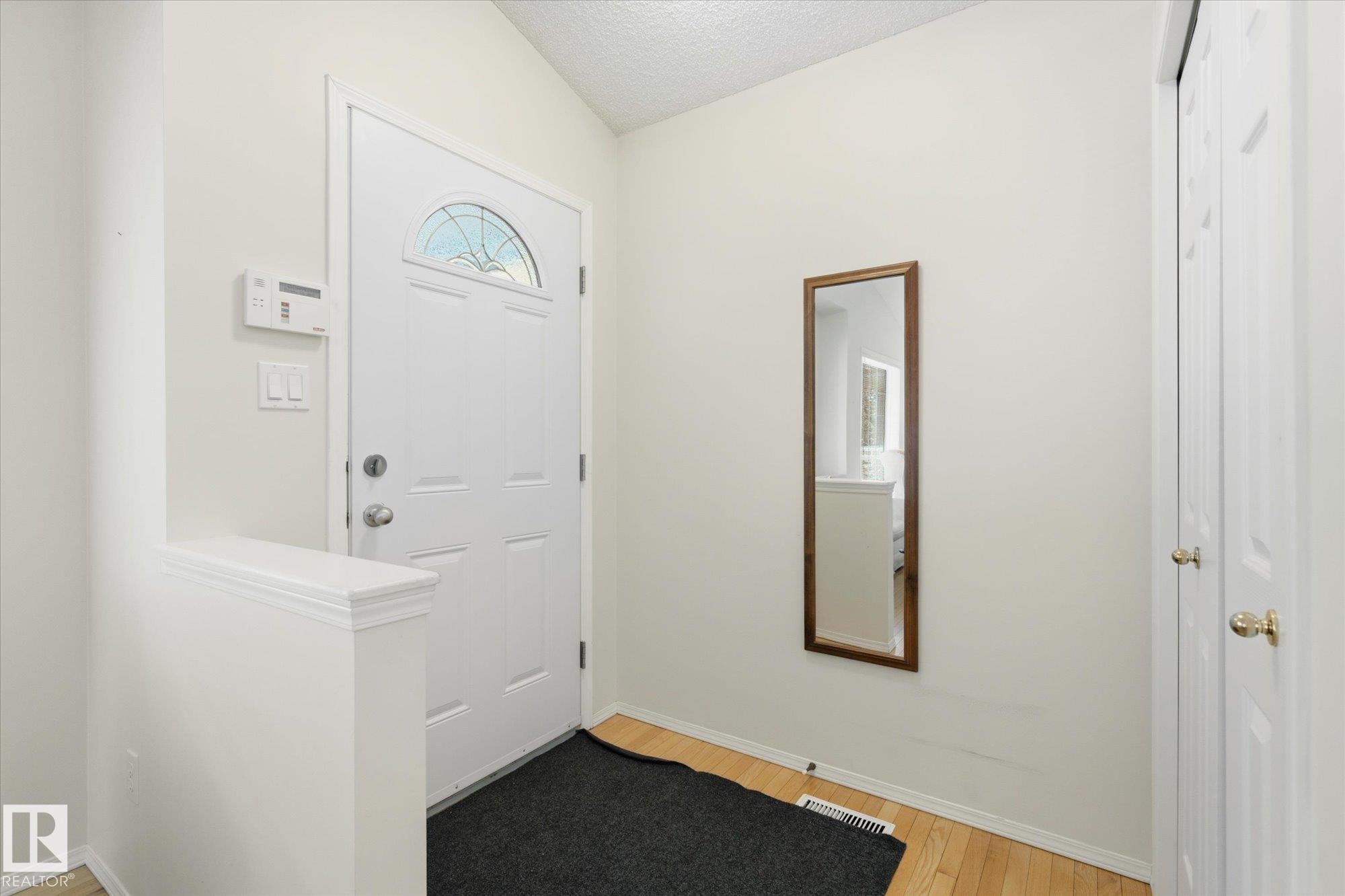 Entryway featuring a white paneled door with an arched stained-glass insert, light wood-finish flooring, and a built-in closet with bifold doors - 1709 Turvey Bend Bend Nw, Edmonton, AB