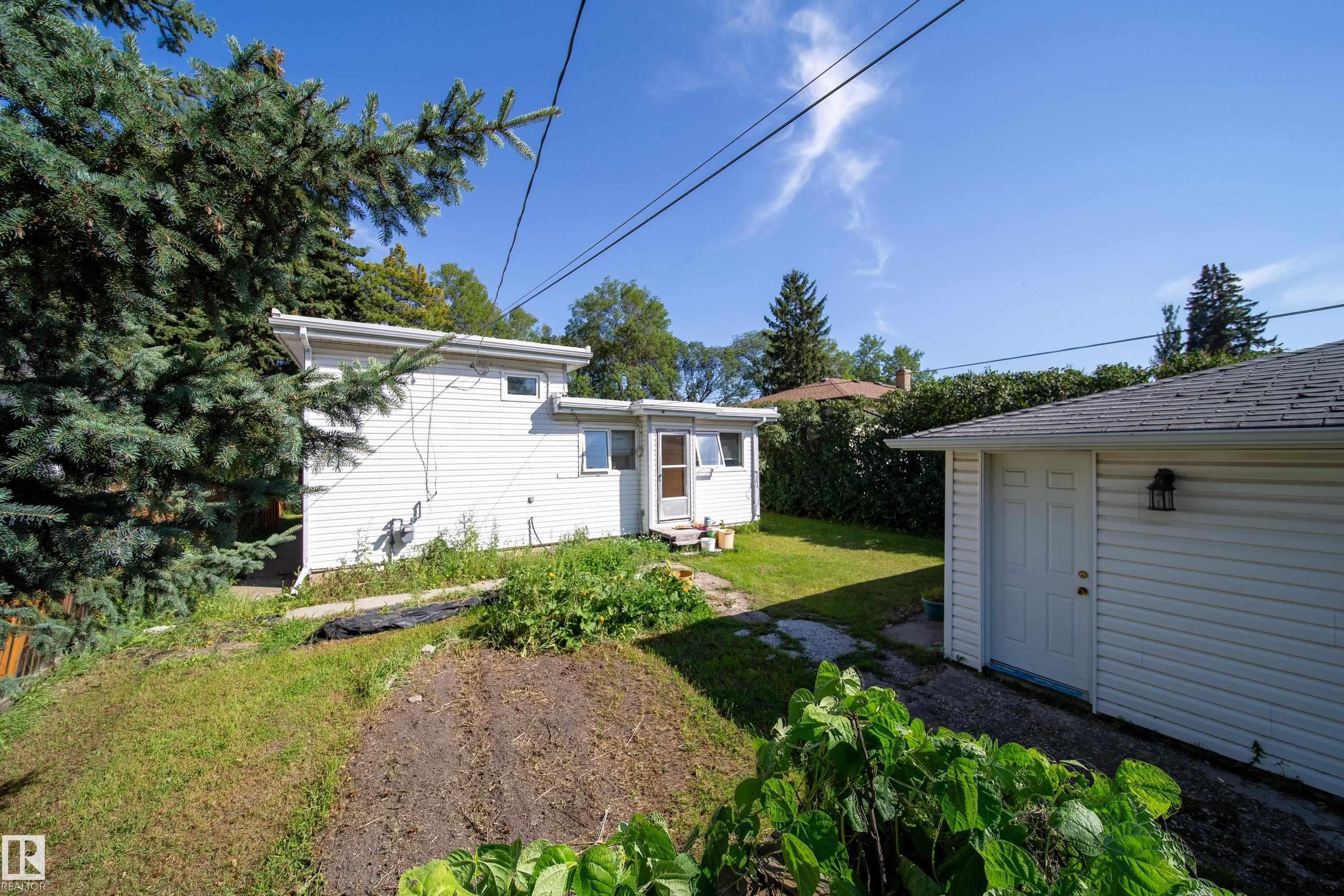 Rear exterior with white siding, detached garage, and mature landscaping - 10738 129 Street Nw, Edmonton, AB