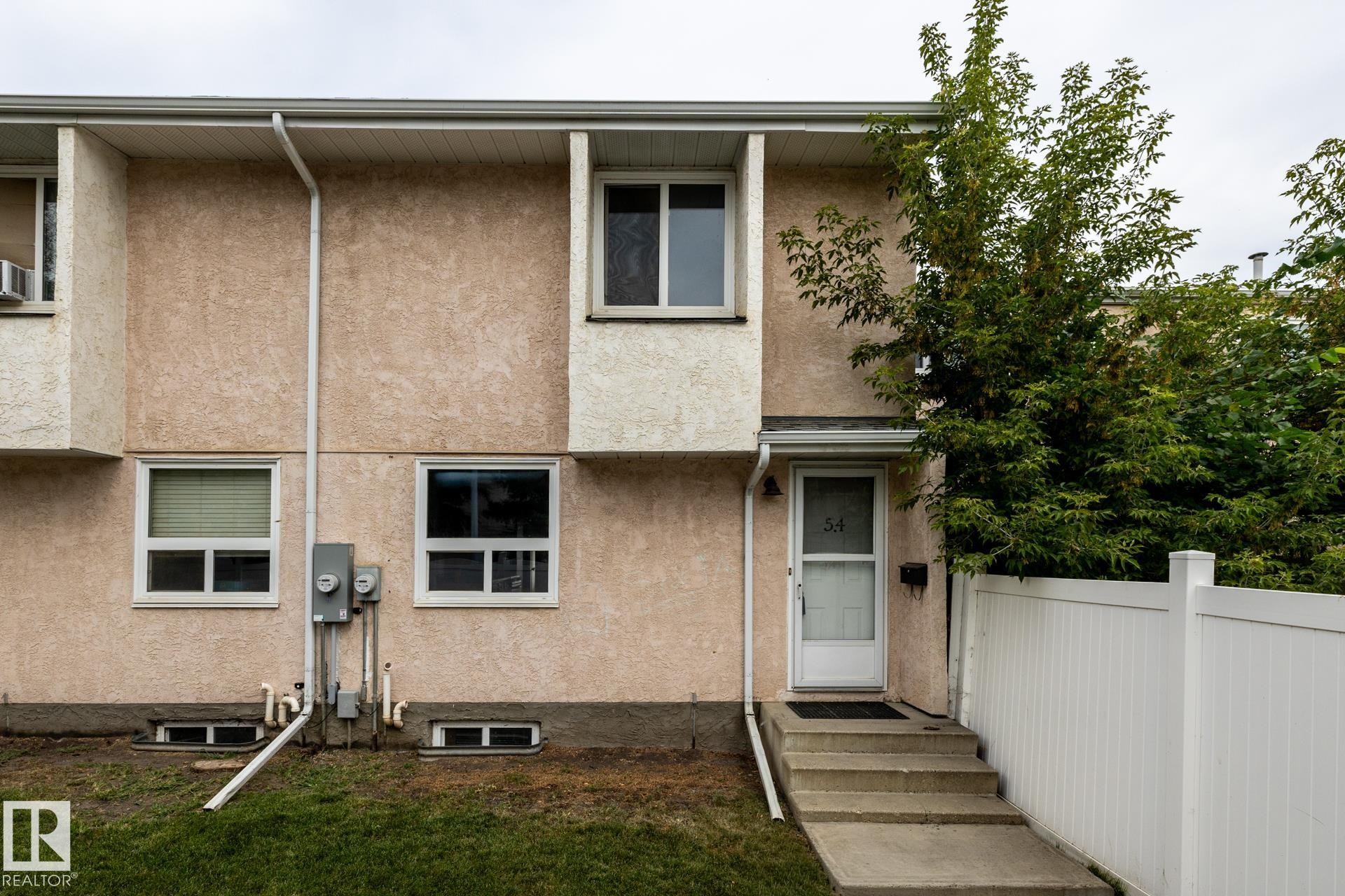 Stucco exterior with white trim windows and a white entry door - 54 Lakewood Village Nw, Edmonton, AB