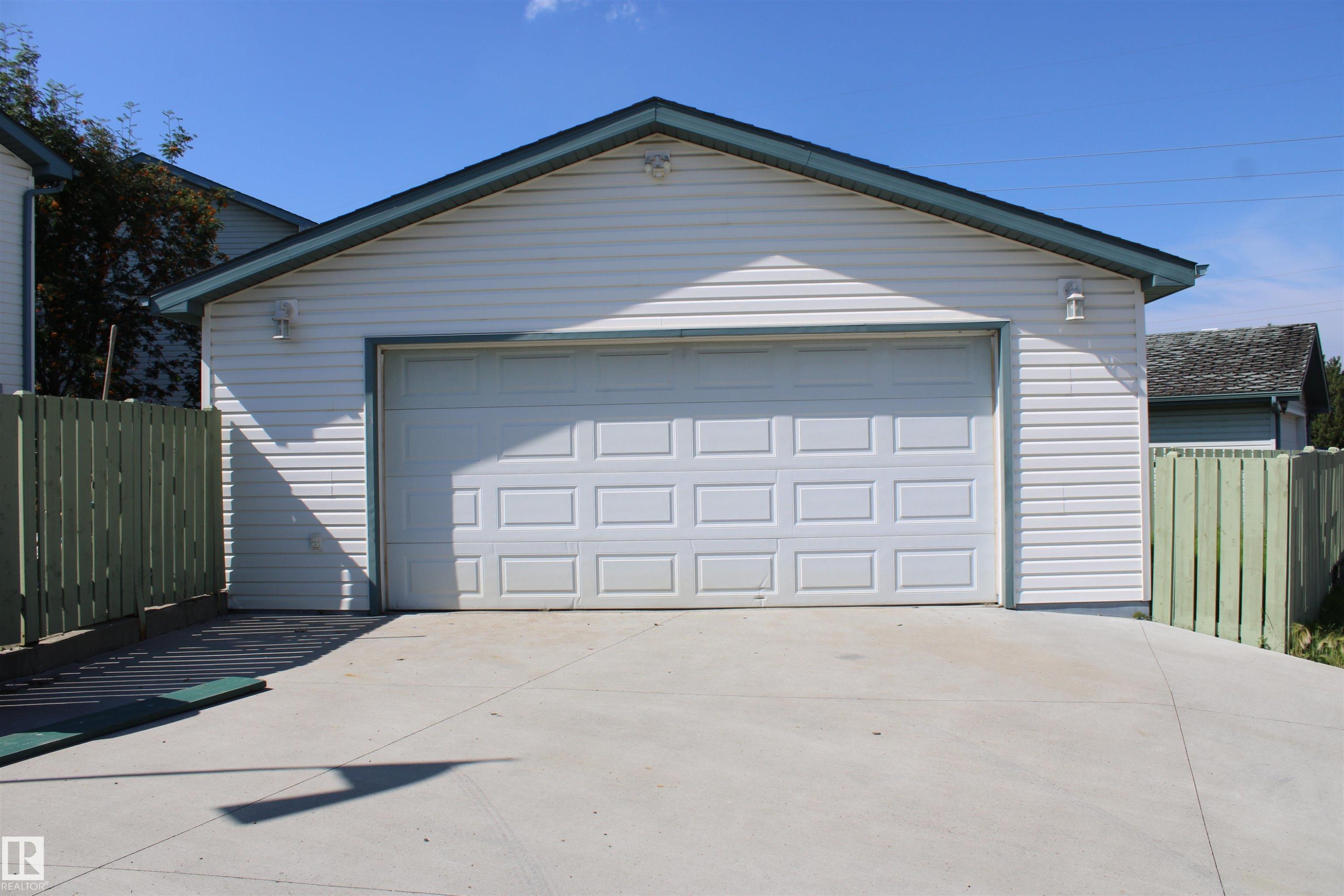 Detached garage with white horizontal siding, a paneled garage door, and a concrete driveway - 15031 135 Street Nw, Edmonton, AB