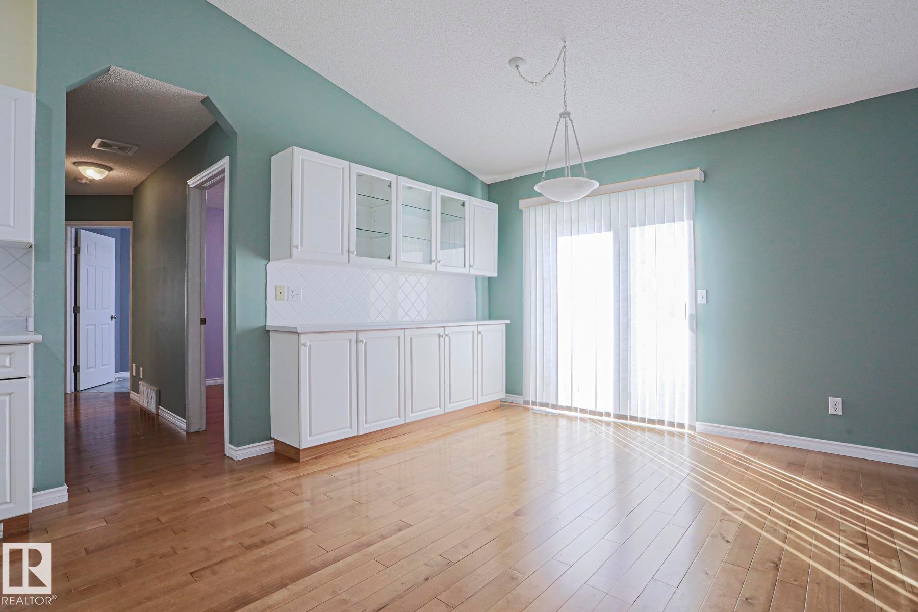 Hardwood flooring, built-in white cabinetry, glass-front upper cabinets, patterned tile backsplash, and a sliding glass door - 15031 135 Street Nw, Edmonton, AB