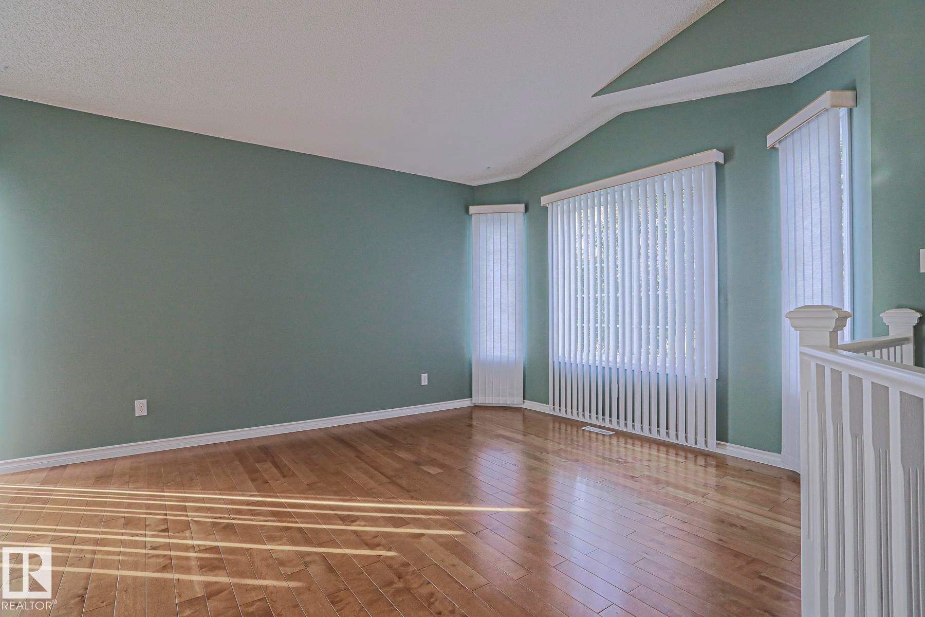 Hardwood-finish flooring, accent wall, multiple windows with vertical blinds, vaulted ceiling, and white railing - 15031 135 Street Nw, Edmonton, AB