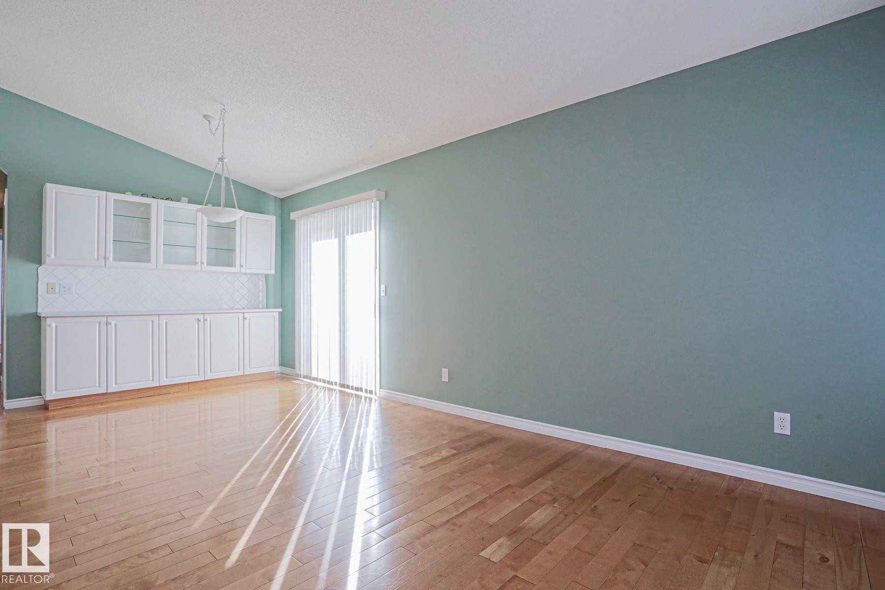 Built-in white cabinetry with glass-front uppers, wood-finish flooring, and a sliding glass door - 15031 135 Street Nw, Edmonton, AB
